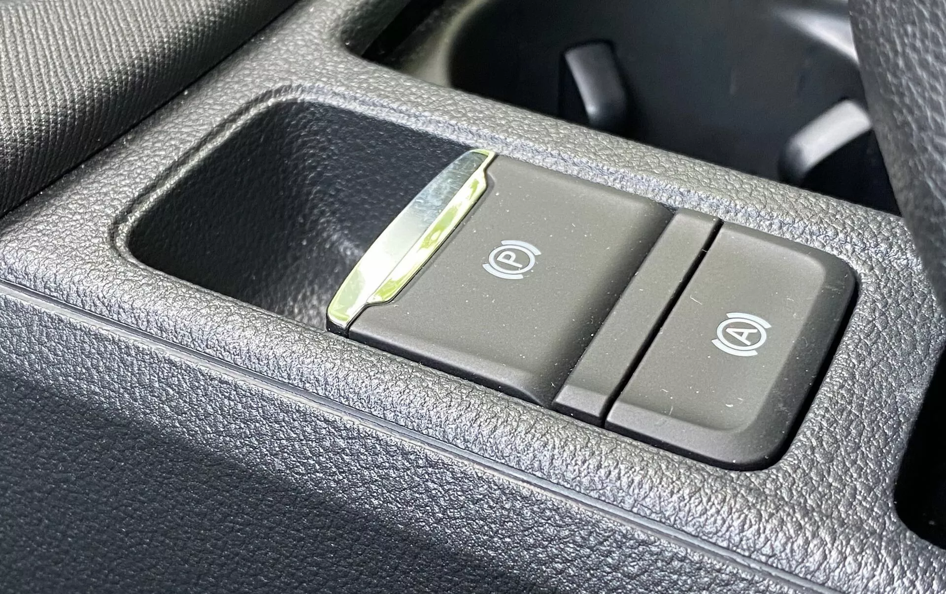 Närbild på kontrollpanelen i Skoda Octavia 2020 inuti fordonet, som visar knappar för uppvärmda och ventilerade säten på ett mörkt, kornigt, läderliknande material. Den vänstra knappen har en ikon för uppvärmt säte, och den högra knappen visar en ikon för ventilerat säte, med en liten LED-indikator mellan knapparna.
