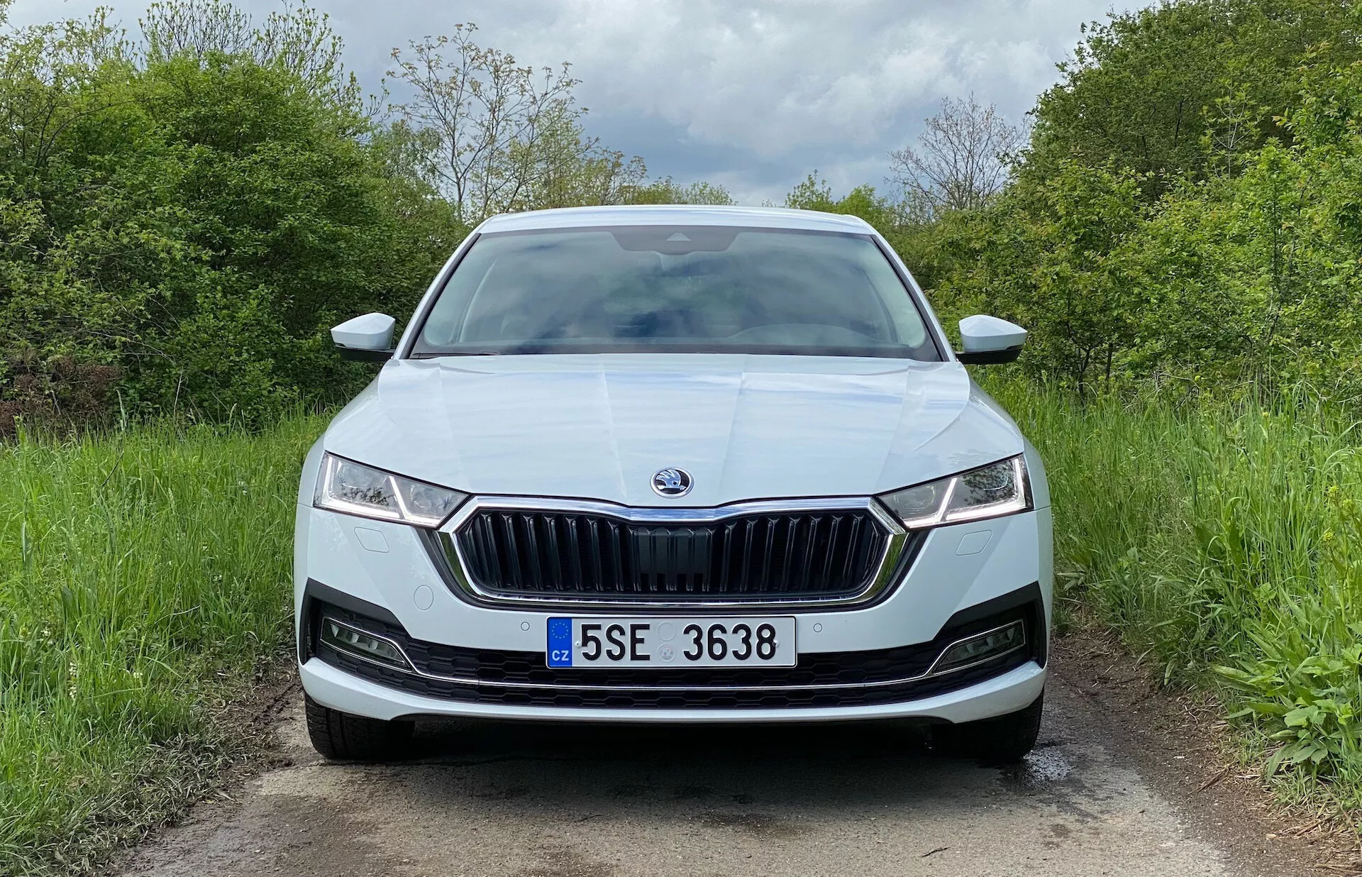 Frontalvy av en Skoda Octavia 2020 sedan på en landsväg som visar den framträdande frontgrillen med vertikala ribbor och kromad kant, smala LED-strålkastare med dagsljus, centralt placerad varumärkesemblem, potentiella parkeringssensorer i stötfångaren, centrerad registreringsskylt, metalliclack, luftintagsventiler och eventuella dimljus.