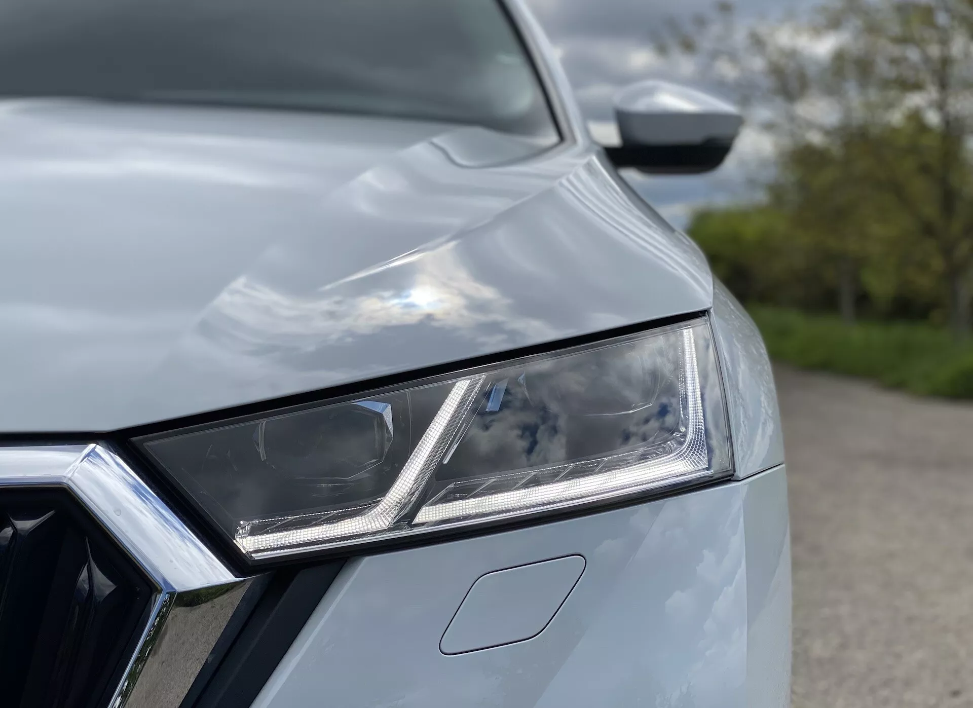 Närbild av en Skoda Octavia Limousine 2020, fokuserad på den intrikata vänstra framstrålkastaranordningen med LED-element och dagsljuslyktor. En del av den kromade frontgrillen är synlig, tillsammans med bilens motorhuv med aerodynamiska linjer, vilket skapar ett modernt, stiligt utseende som indikerar premiumteknologi och design.