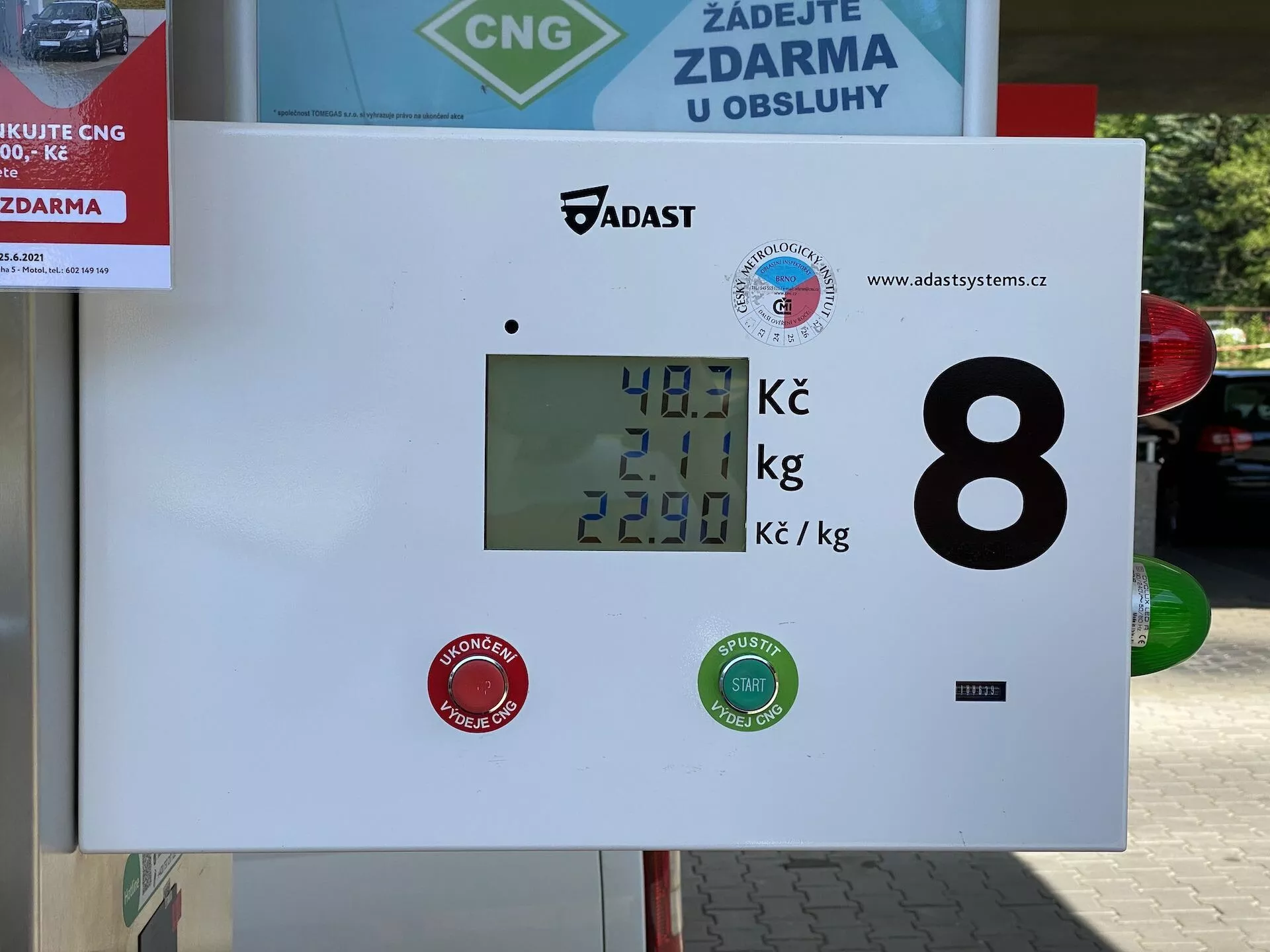 Display av en komprimerad naturgas (CNG) bränsleautomat på en bensinstation som visar 40,1 Kč för mängden bränsle, 2,01 kg som gasens vikt och ett pris per kilogram på 22,90 Kč. Displayen inkluderar varumärkeslogotyper och ett numeriskt identifikationsnummer 8, med en utomhusmiljö indikerad av en biltvätts- eller servicemärkning i bakgrunden.