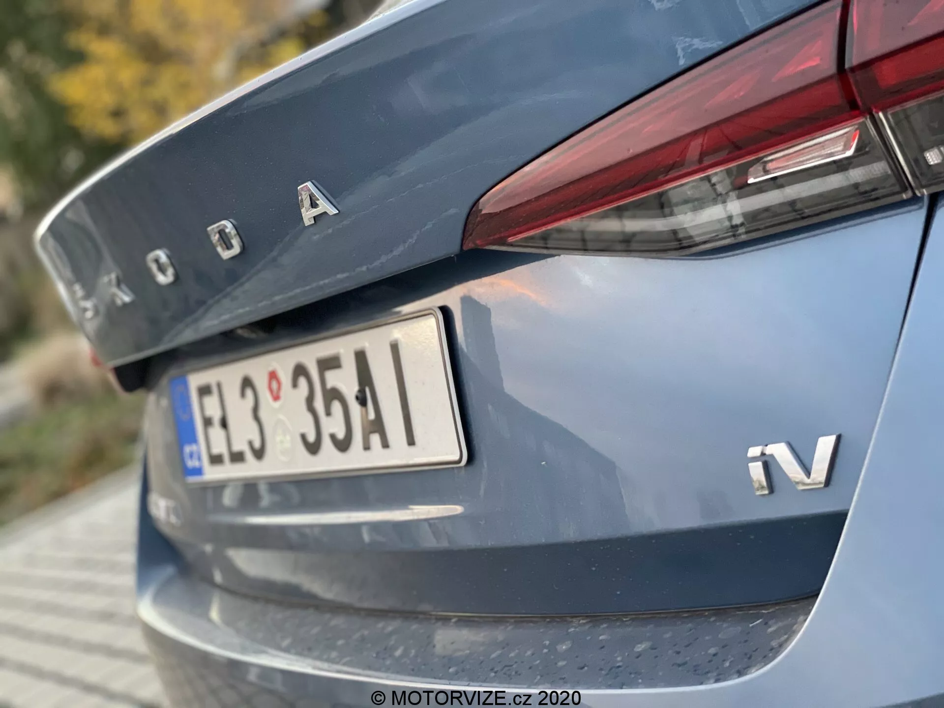 Närbild av bakre delen av en 2020 Škoda Octavia Limousine, tagen från en låg vinkel med fokus på bagageluckan, bakre stötfångaren och med kromade Škoda-logotypen, iV-märke för hybrid- eller eldriven variant, europeisk stil registreringsskylt, smala horisontella bakljus som sträcker sig till bagageluckan, och en reflekterande remsa på bakre stötfångaren.