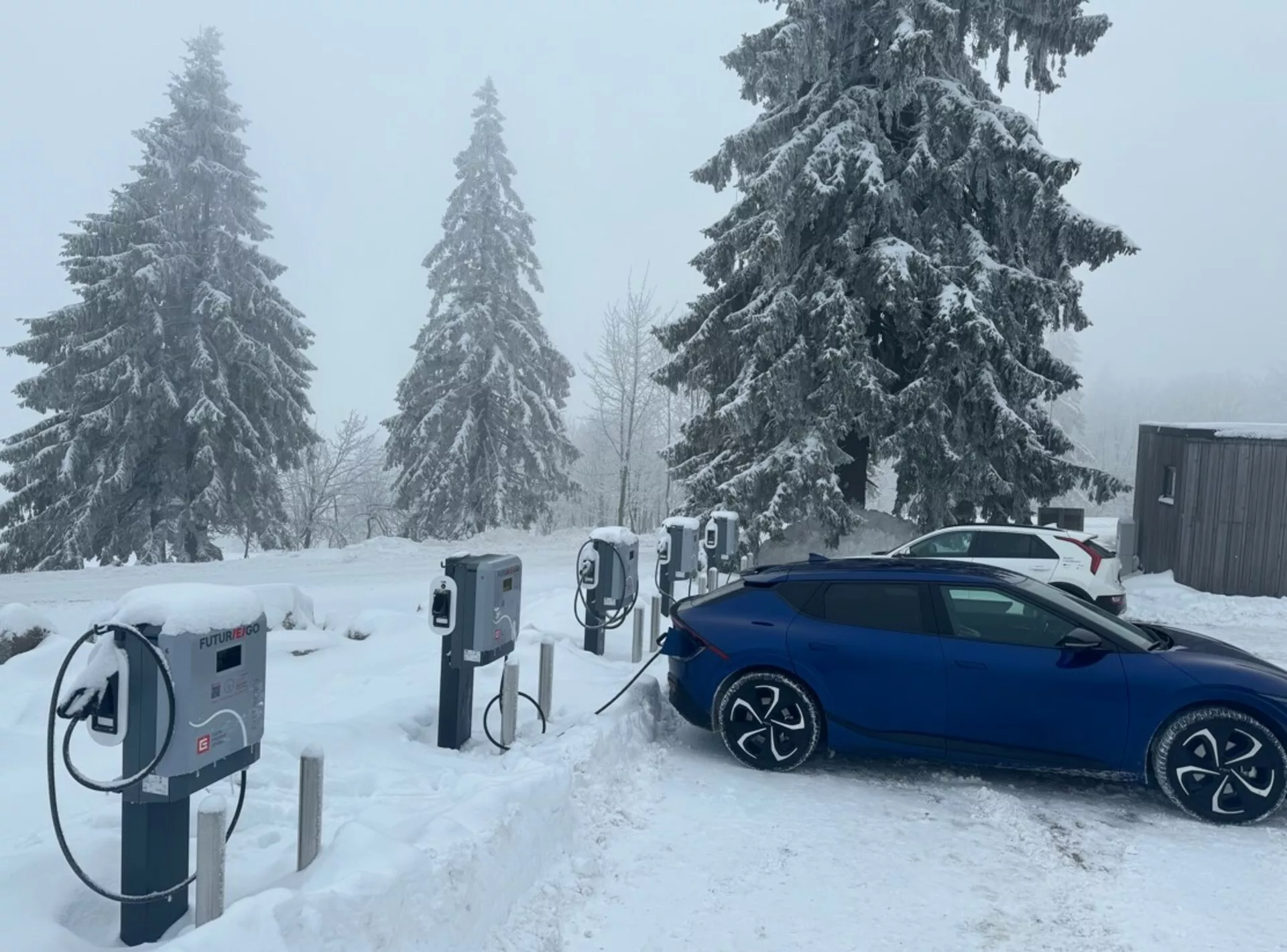 Blå Skoda Octavia Limousine 2020 som laddar vid en elbilsladdningsstation, ses diagonalt från baksidan, framhäver dess legeringshjul, laddningsport och vinterklara design bland snöiga förhållanden.