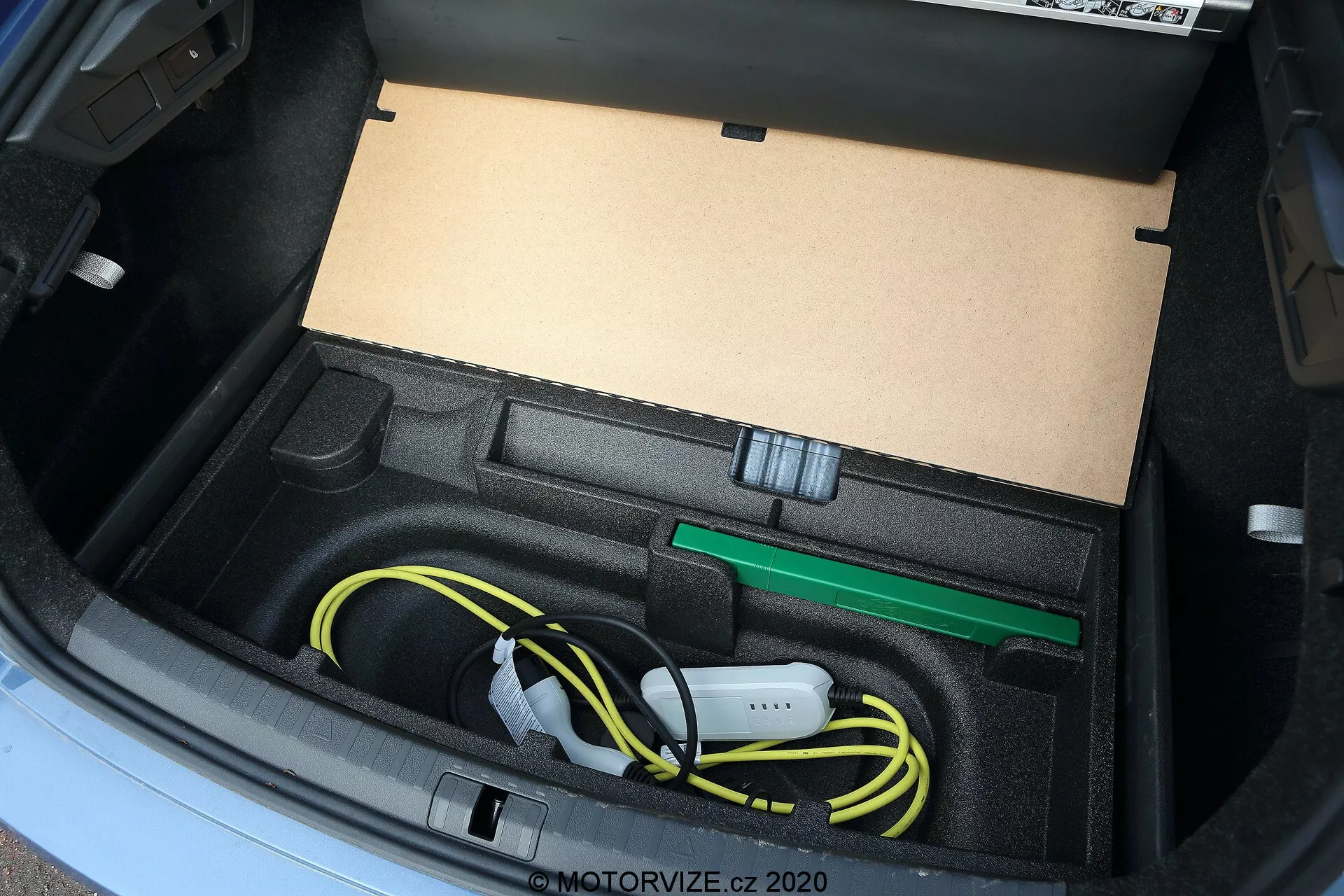 Närbild av bagageutrymmet i Skoda Octavia 2020, som visar ett skräddarsytt fack designat för att förvara elfordonets laddkabel och tillbehör, inklusive en noggrant ihoprullad gul laddkabel och en grön bogserögla, fotograferat från en hög vinkel med naturligt ljus.