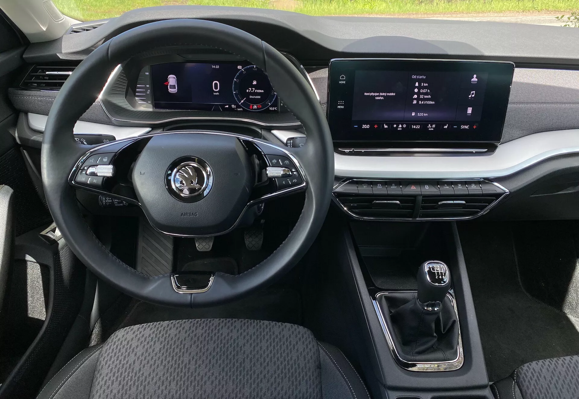 Interiörvy av 2020 Škoda Octavia sedan från passagerarsätets perspektiv, framhävande en multifunktionell tre-ekrad ratt med olika kontroller för media och handsfree-samtal, en digital instrumentpanel för navigering och fordonsstatistik, en central infotainment-pekskärm, en kompakt automatisk växelspak, metalliska detaljer på luftventiler och infotainmentsystem, slitstark tygklädsel på förarsätet och justerbar ambient belysning.