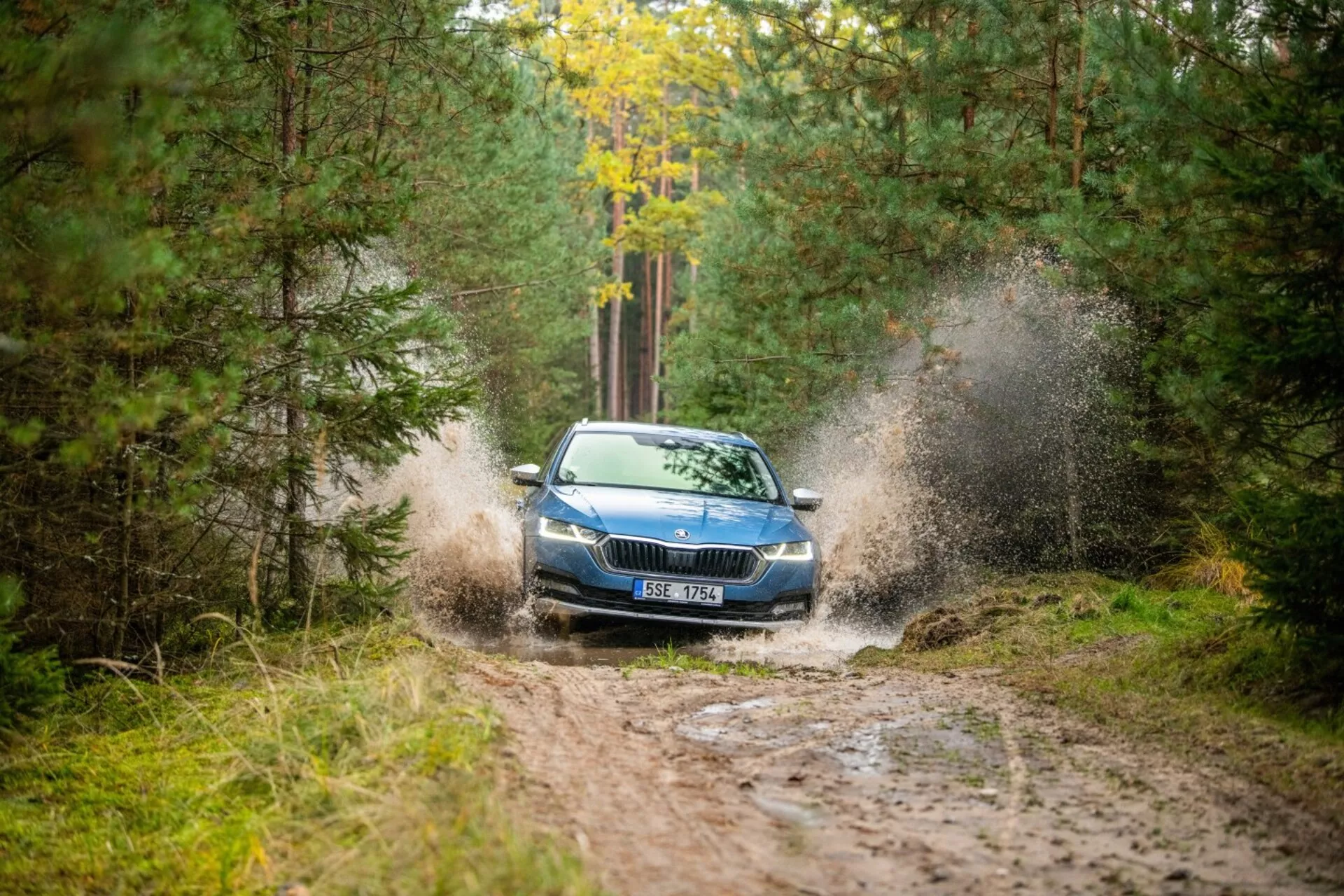 2017 Skoda Octavia limousine kör genom en lerig pöl i ett skogsområde, med fokus på dess dynamiska skapande av stänk, frontgaller, strålkastare och huven med en delvis vy av taket från en främre höger vinkel.