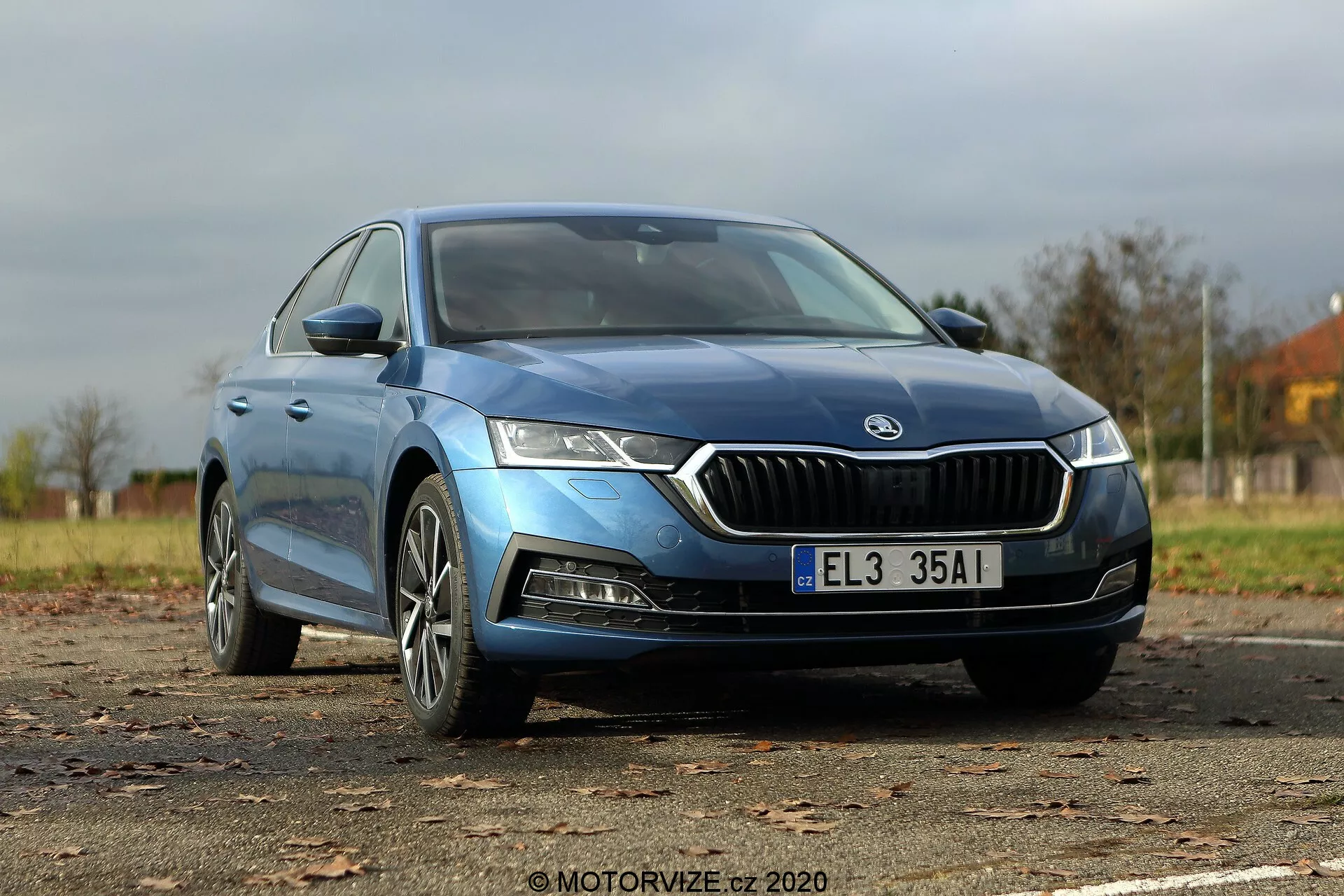 Bild av en blå Škoda Octavia Limousine 2020 tagen från en låg fram-trekvarts vinkel, som framhäver den distinkta kromomgivna frontgrillen, skarpa LED-strålkastare, konturerad motorhuv, moderna lättmetallfälgar och eleganta sidospeglar med integrerade blinkers. Den släta karossen och de lätt tonade ramlösa fönstren antyder en högre utrustningsnivå, medan hela bilens längd visas, inklusive synliga märken som indikerar modell eller motortyp.