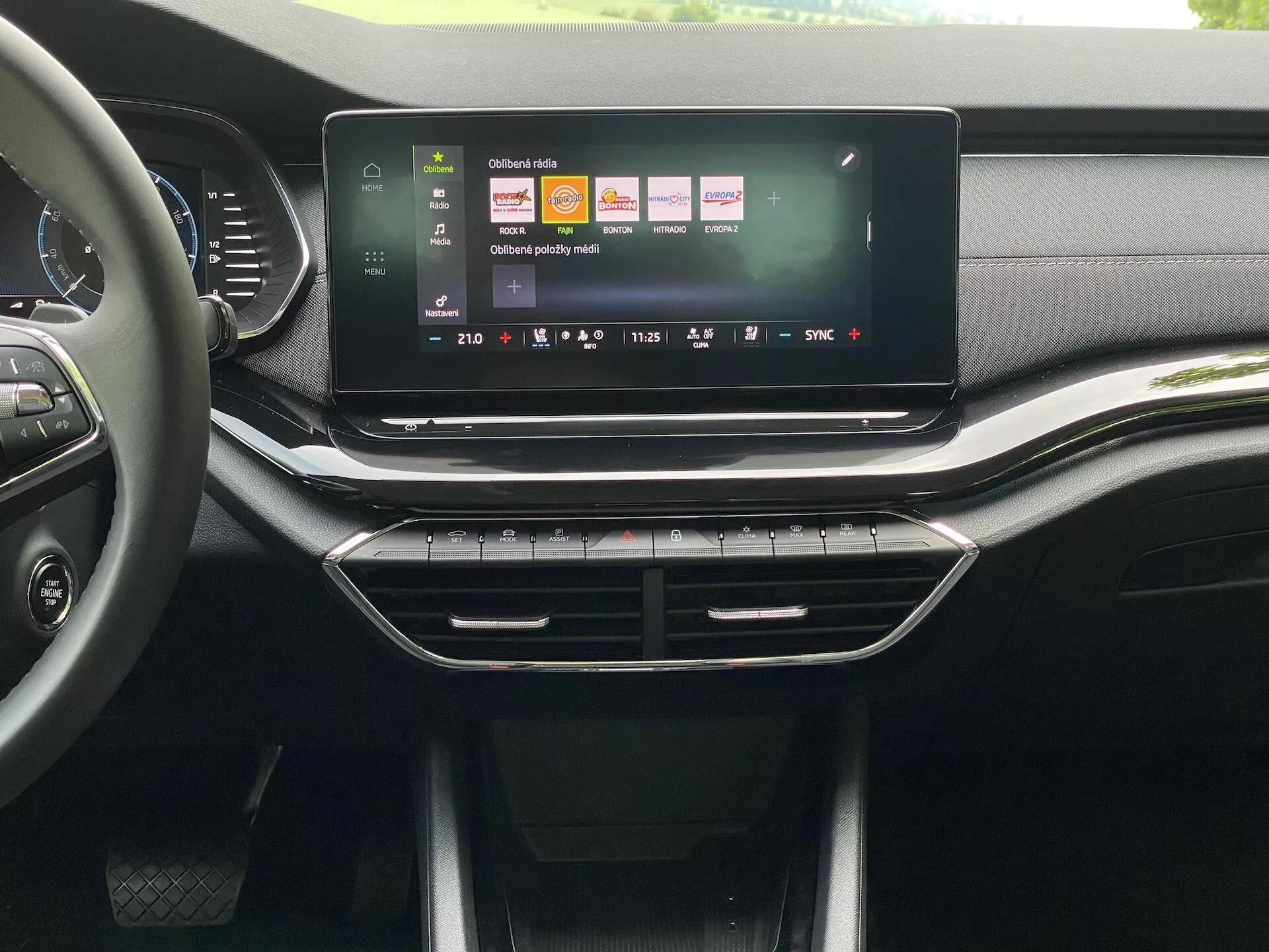 Interiör av Škoda Octavia 2020 limousine, som framhäver den centrala konsolen och infotainmentsystemet från ett framsätesperspektiv. Den stora, landskapsorienterade pekskärmen visar en livfull användargränssnitt med ikoner för navigation, medieuppspelning och fordonsinställningar. Under pekskärmen finns strömlinjeformade luftventiler med dekorativ kromkant, följt av fysiska knappar och reglage för klimatsystemet. Instrumentbrädan och konsolen har en blandning av läderliknande texturer och matta och glansiga plaster, vilket tyder på en högkvalitativ design för mellanklass till övre marknadssegmentet.