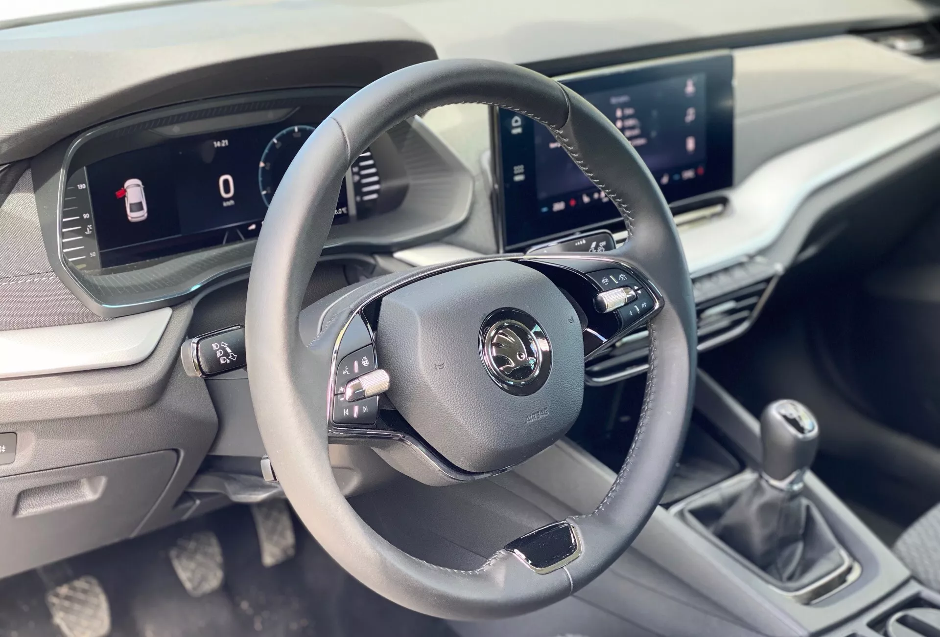 Interiörbild av 2020 Škoda Octavia limousin fokuserad på förarområdet, med en treekrad läderklädd ratt med kontrollknappar, digital instrumentpanel och centralt infotainmentsystem från framsätespassagerarens synvinkel.
