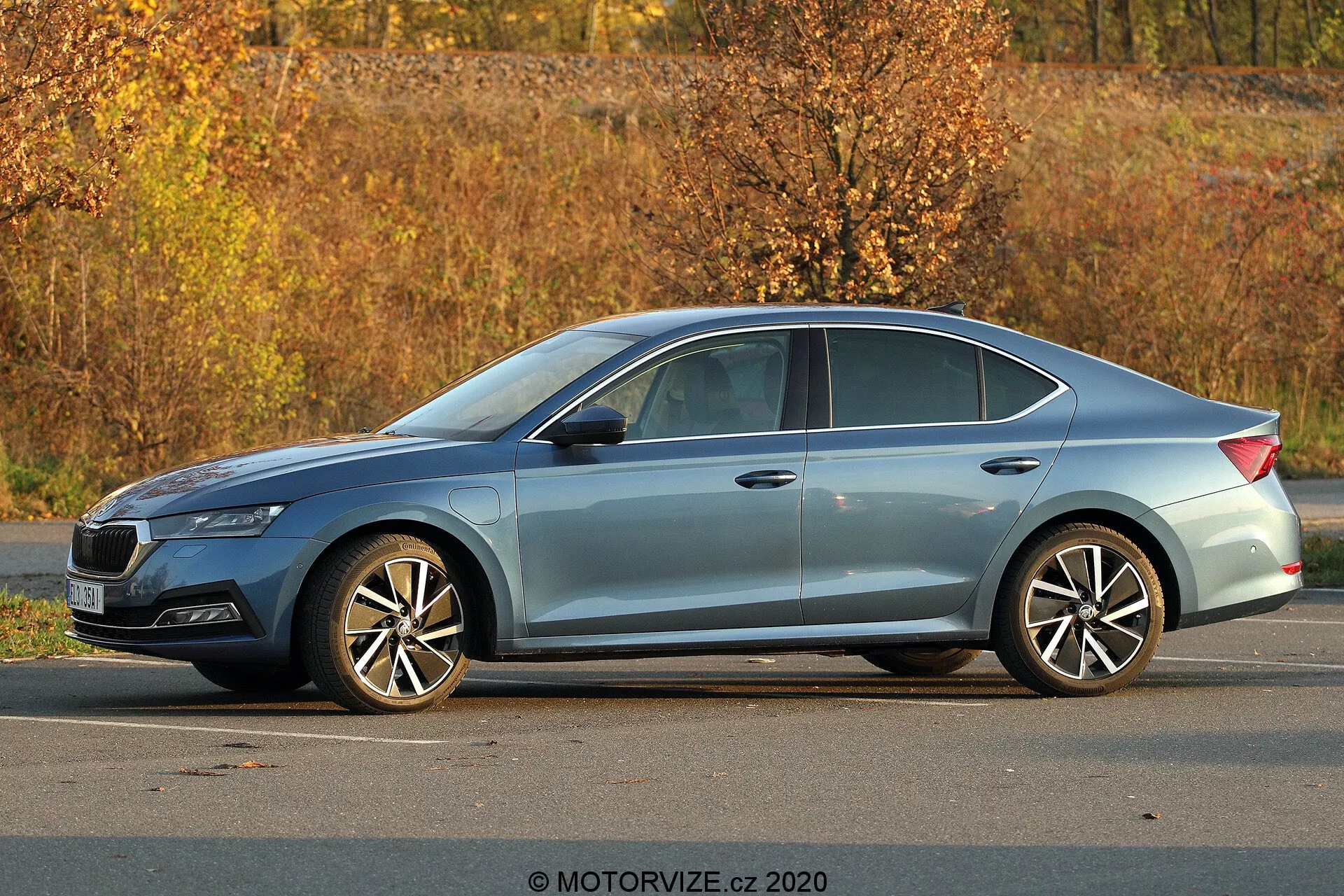 Modern Skoda Octavia 2020 sedan parkerad utomhus, trekvarts sidovy som visar full profil, längd och höjd; synliga detaljer inkluderar skarpa strålkastare, sluttande taklinje, karaktärslinjer, krominfattade fönster, fler-ekrade aluminiumfälgar, höstlig lövomgivning och naturlig dagsljusbelysning.