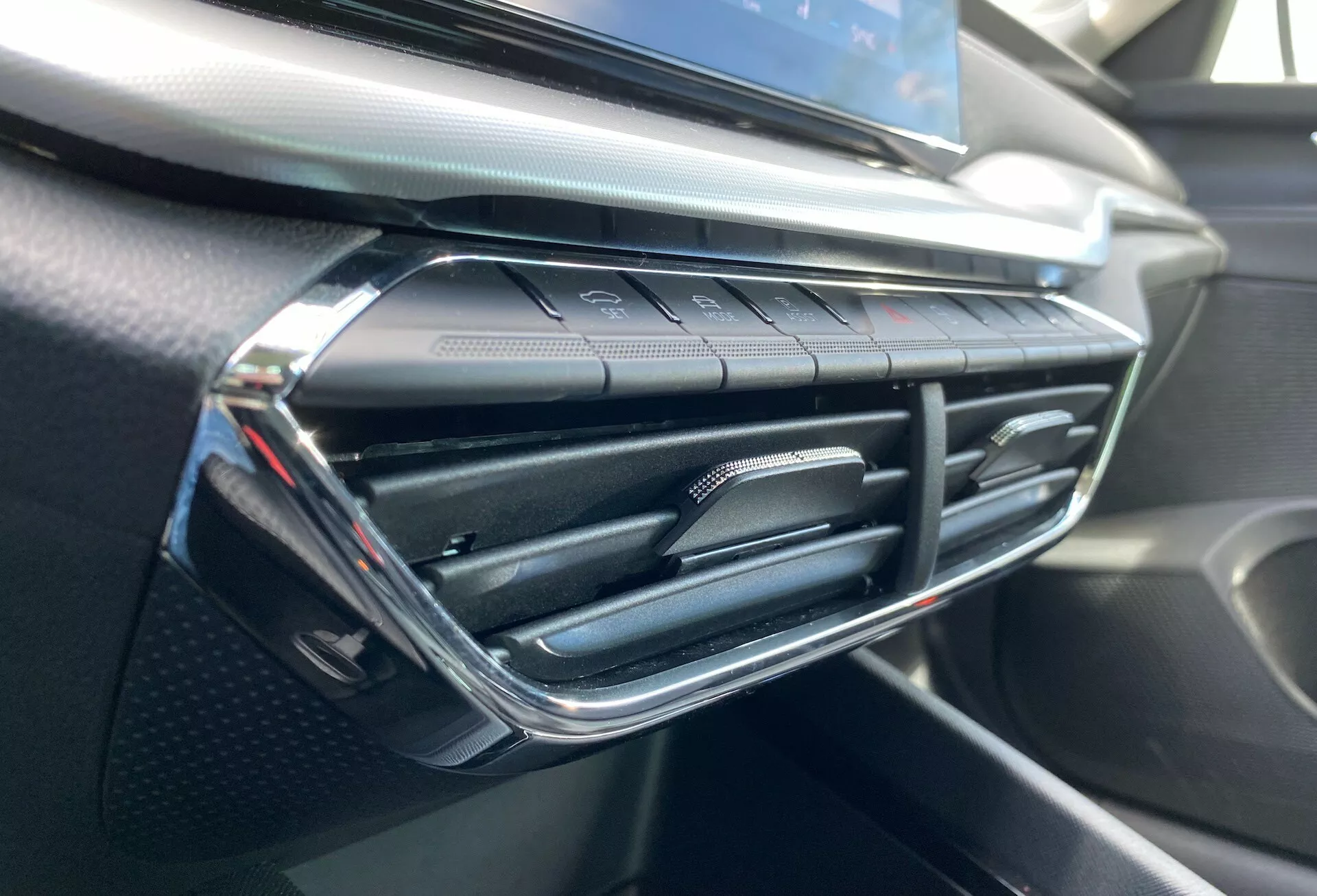 Närbild av interiören i Skoda Octavia 2020 som framhäver luftkonditioneringsventilen och området runt instrumentbrädan, med en modern ventildesign med kromdetaljer och tryckkänsliga klimatkontrollknappar nedanför, på en instrumentbräda med mjuk känsla och kolfiberliknande textur.