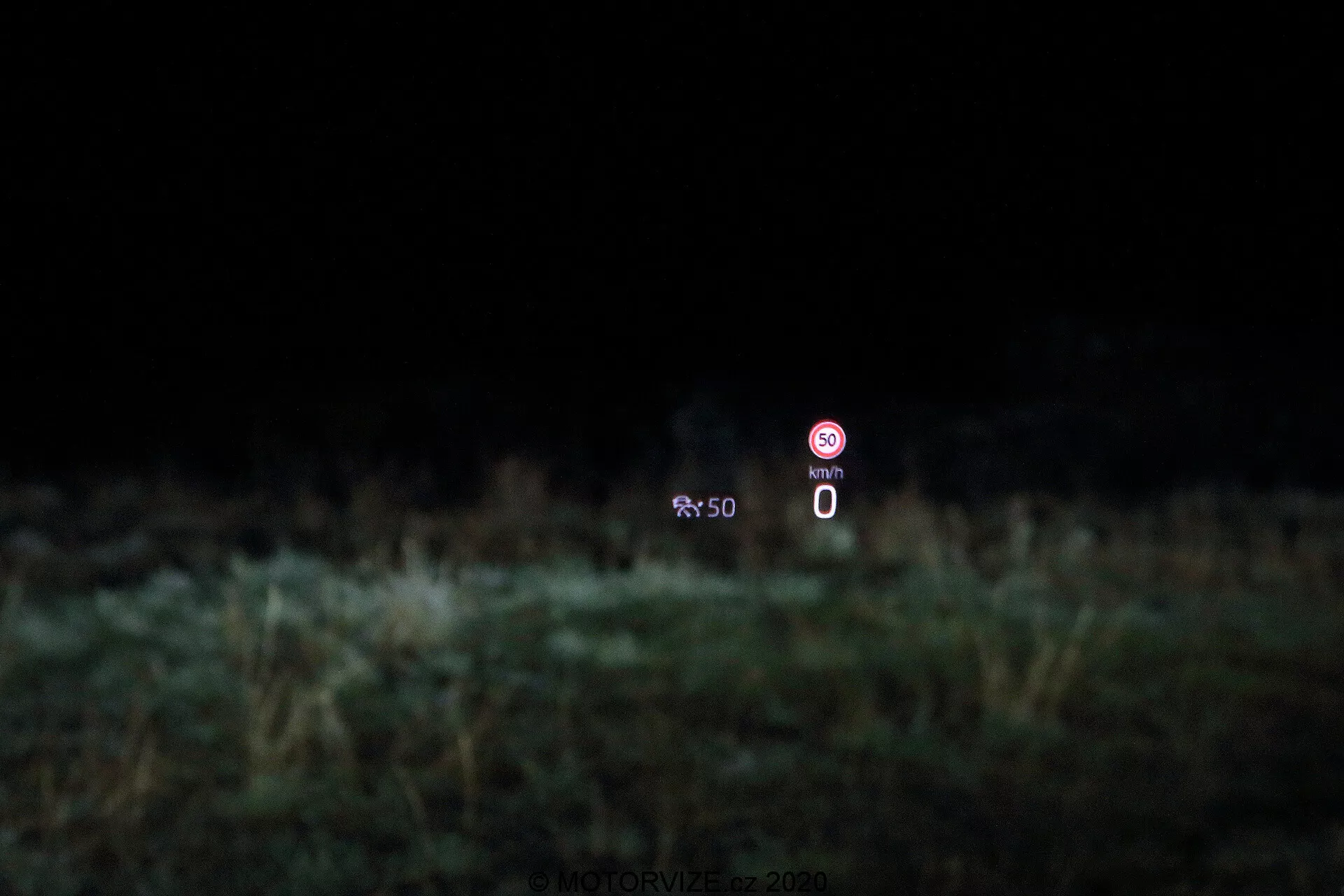 Bild som visar head-up display (HUD) teknologi i en Škoda Octavia 2020 limousine. Displayen projiceras på vindrutan och visar en statisk hastighetsmätare på 0 km/h samt en förbudssymbol som indikerar en avstängd funktion, mot en suddig bakgrund av växtlighet.