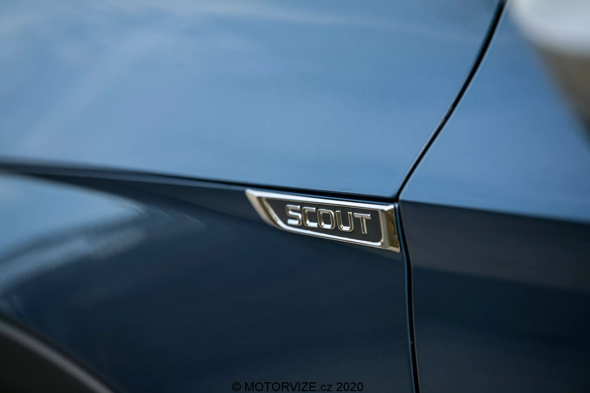Närbild av en SCOUT-märke på en mörkblå Škoda Octavia 2020, som visar bilens specialutgåva med glänsande silverbokstäver på en svart bakgrund, vilket återspeglar den lyxiga detaljeringen och den polerade lacken.