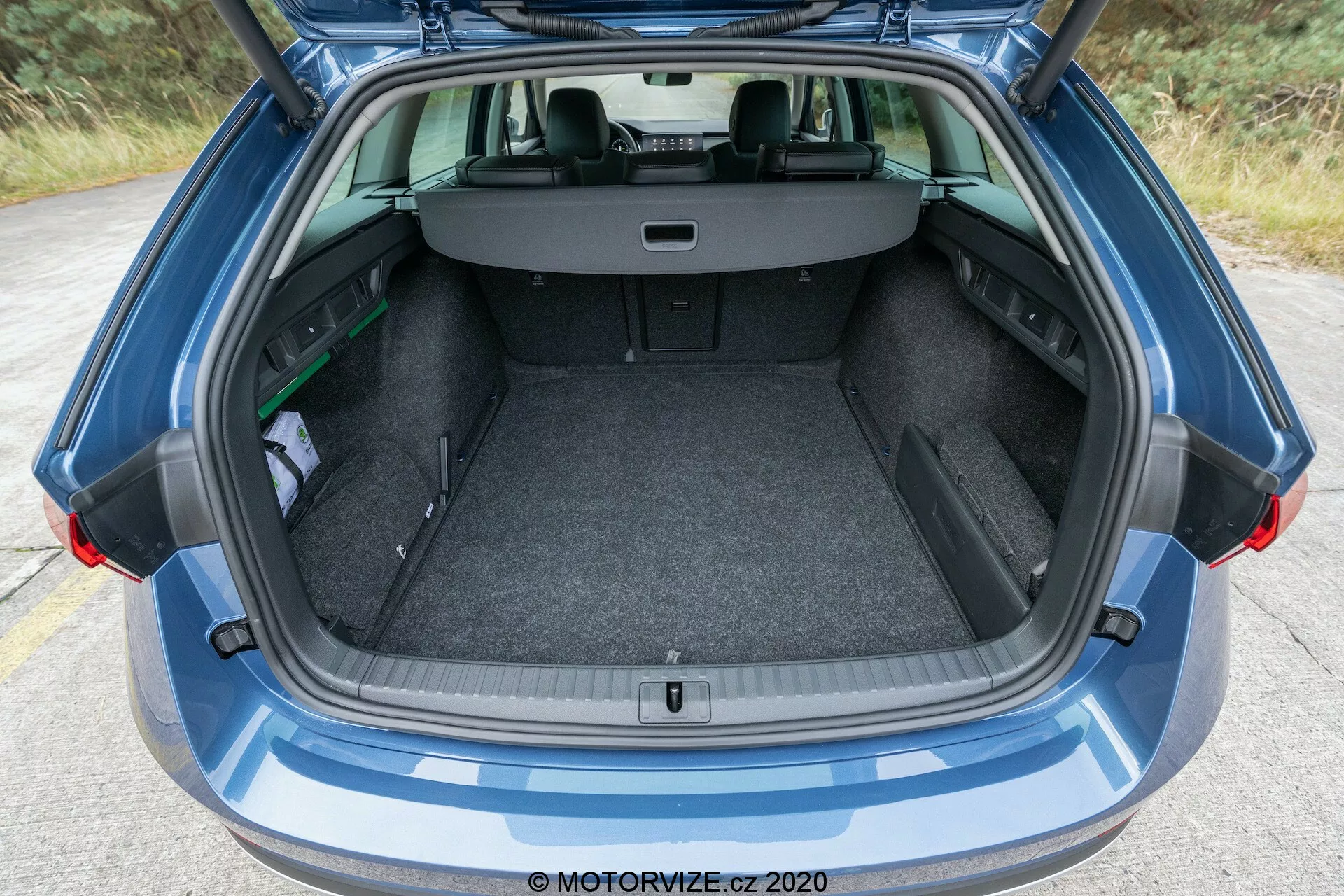 Närbild av den öppna bagageutrymmet på en modern Skoda Octavia Scout 2020, med en fullt öppen bakluckedesign. Bilden fångar bagageutrymmet från den bakre stötfångaren till den bakre vindrutan, inklusive en del av taket. Det matta klädda lastutrymmet har en plan lastyta och ett litet förvaringsutrymme till vänster. Baksätena är i vanligt sittläge med ett utdragbart lastskydd utsträckt, vilket döljer föremålen i bagageutrymmet.