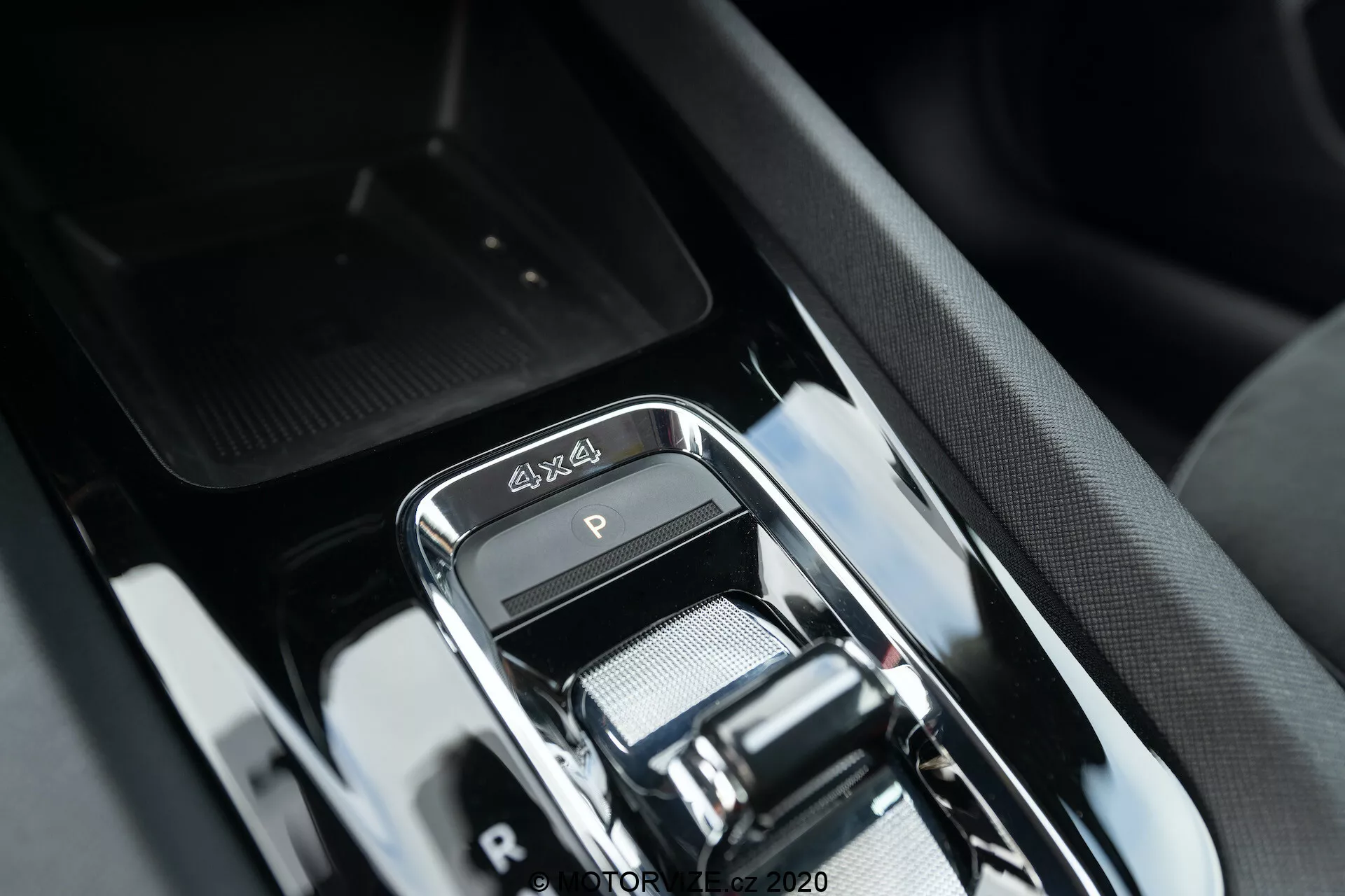 Närbild av växelspakens område i den lyxiga interiören på Skoda Octavia Scout 2020, och visar en modern elektronisk växelväljare med kromfinish, 4x4-emblem, elegant högblank svart trim och sofistikerad design på mittkonsolen med omgivande knappar och antydd förvaringsfack.