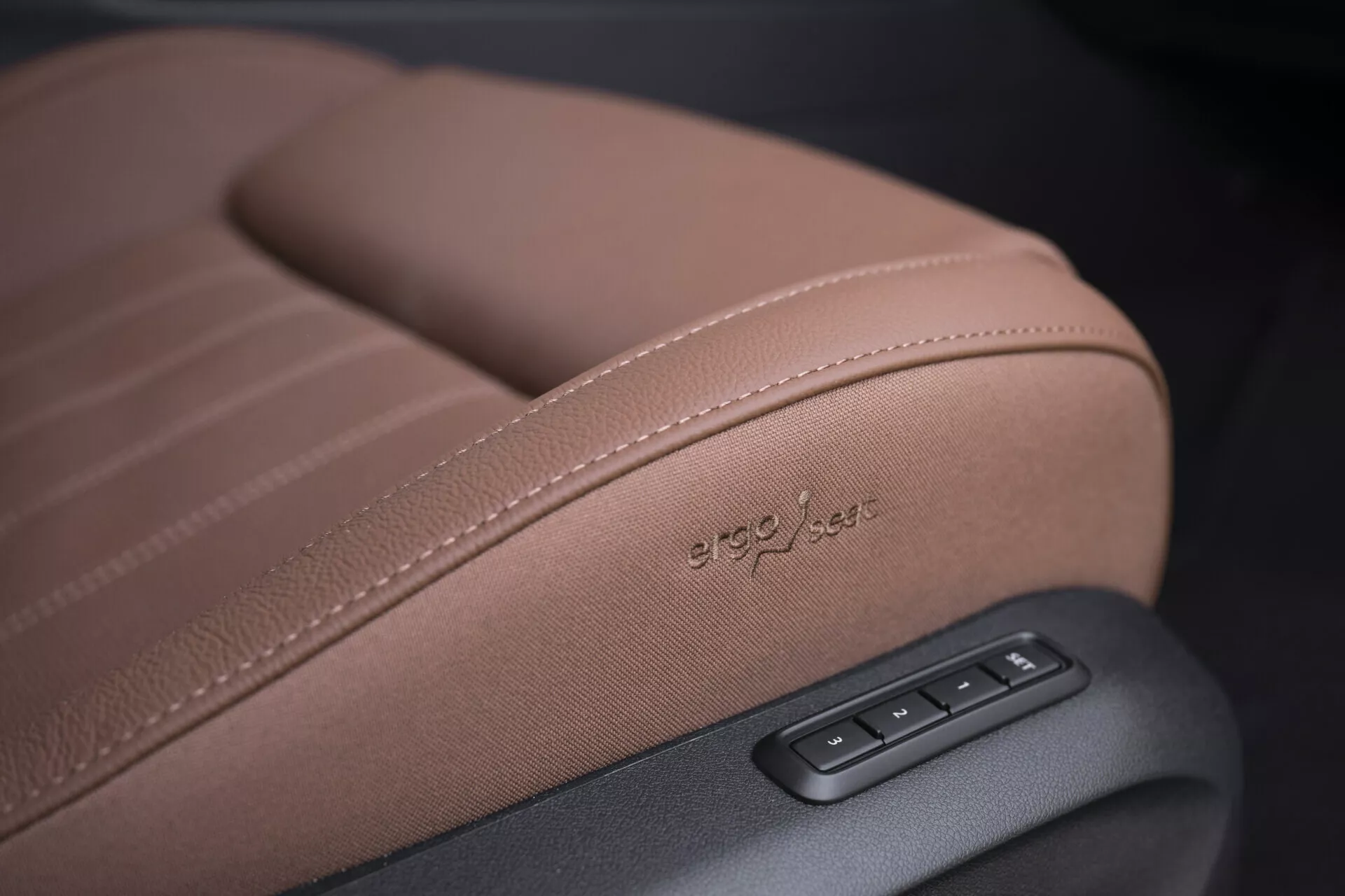Närbild av ett säte i en Skoda Superb 2024 Combi som visar detaljerad sömnad, 'ergo-jets' präglat klädsel och elektroniska justeringskontroller i högkvalitativt brunt läder