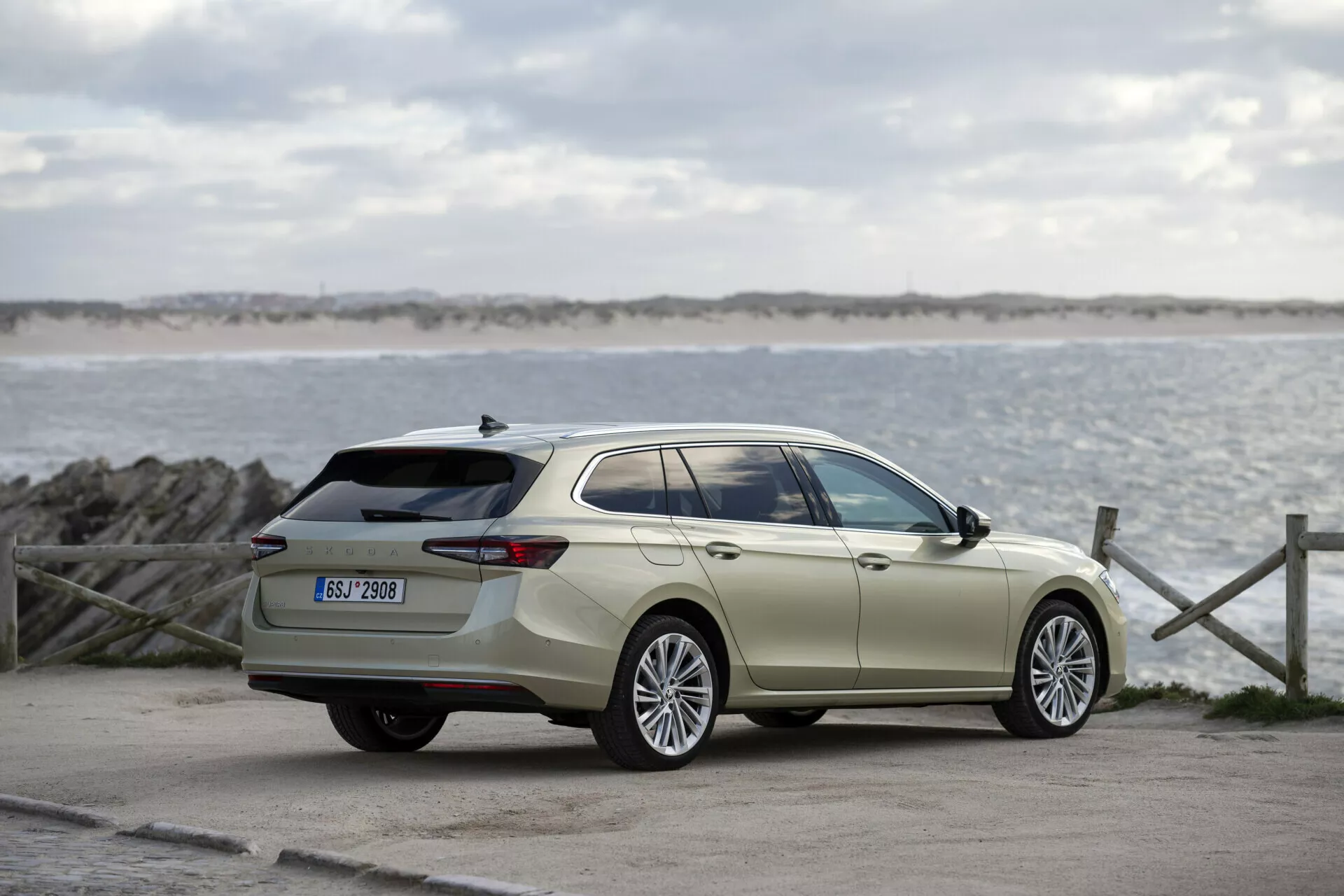 Skoda Superb Combi 2024 i utomhusmiljö med hav och himmel i bakgrunden, visar full sidoprofil, stora legeringshjul, karossfärgade dörrhandtag och speglar, kromad fönsterlist, förlängd taklinje, aerodynamiska kroppskonturer och takräcken