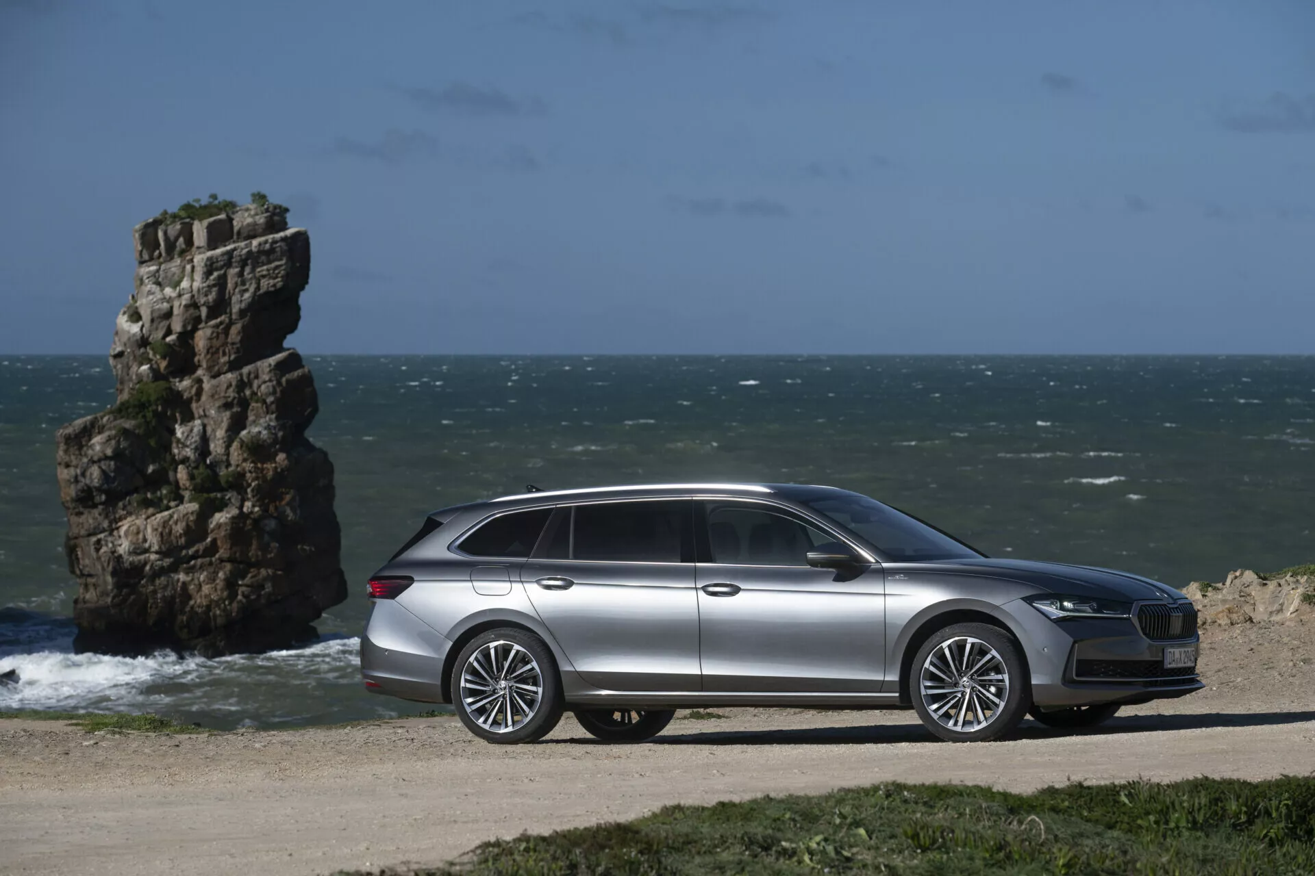 2024 Skoda Superb Combi parkerad vid oceanen med sidosiktsprofil som visar design- och tekniska funktioner, med naturligt havslandskap i bakgrunden