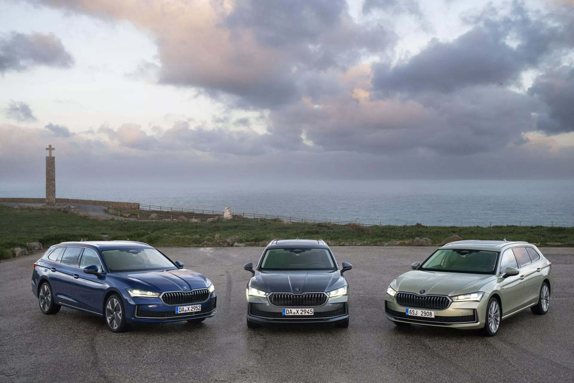 2024 Skoda Superb Combi-modeller parkerade i rad inför kameran vid soluppgången, med fokus på deras grillar, strålkastare och sidoprofiler mot en kustnära landskap
