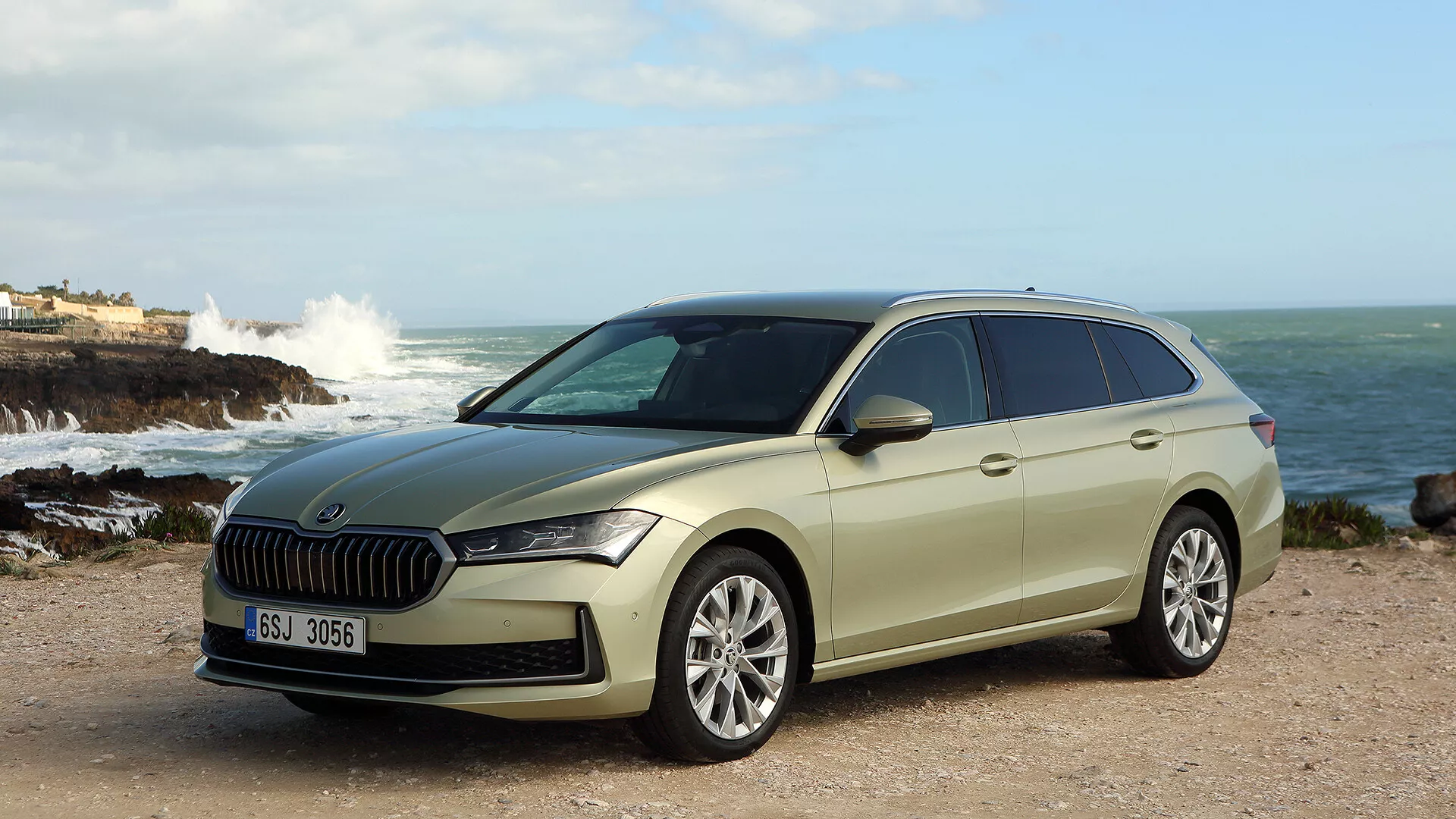 Skoda Superb Combi 2024 visas upp i en naturlig kustinställning, med en framträdande grill, slanka LED-strålkastare, avancerade förarassistanssystem och en stilren men praktisk design med legeringshjul och takräcken