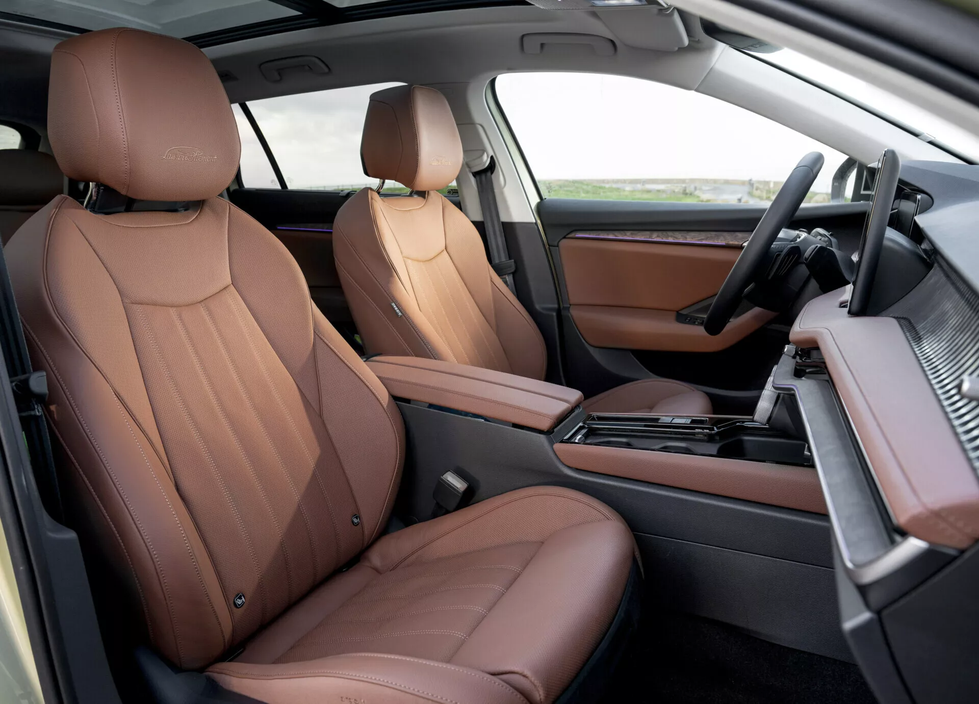 Lyxiga bruna lädersäten och modernt instrumentbräda i frontkabinen på Skoda Superb Combi 2024, som visar automatlåda, infotainmentsystem och träslagsaccenter från en övre passagerarperspektiv