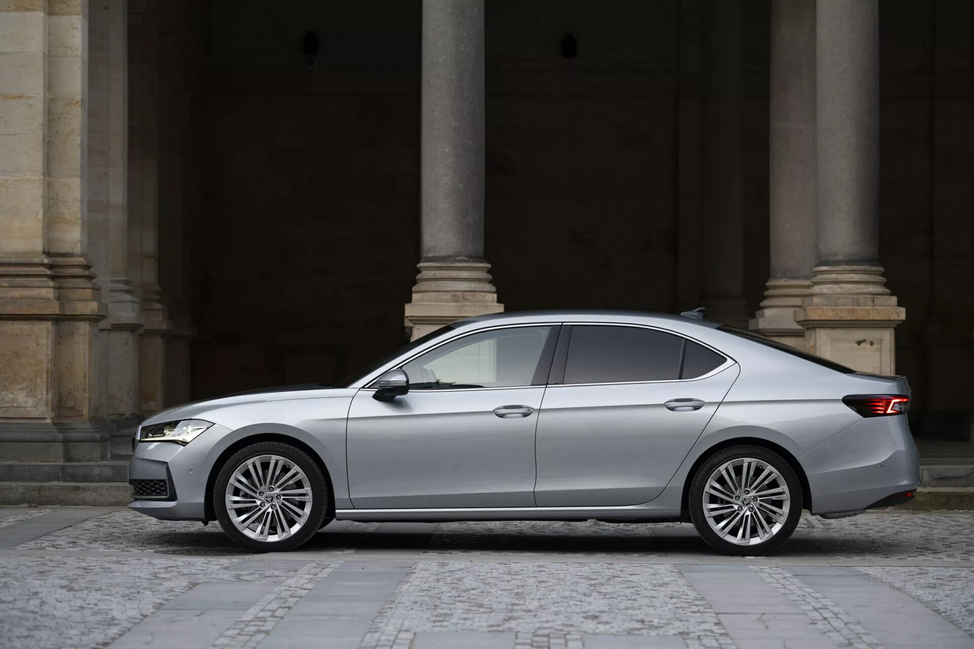 Sidoprofilvy av 2024 Skoda Superb Limousine, fyradörrars sedan i silver/grå, med kantiga LED-strålkastare, strömlinjeformad grill, tonade rutor, karaktärslinje genom dörrhandtagen, flerspakiga lättmetallfälgar och baklyktor som sveper runt hörnen.