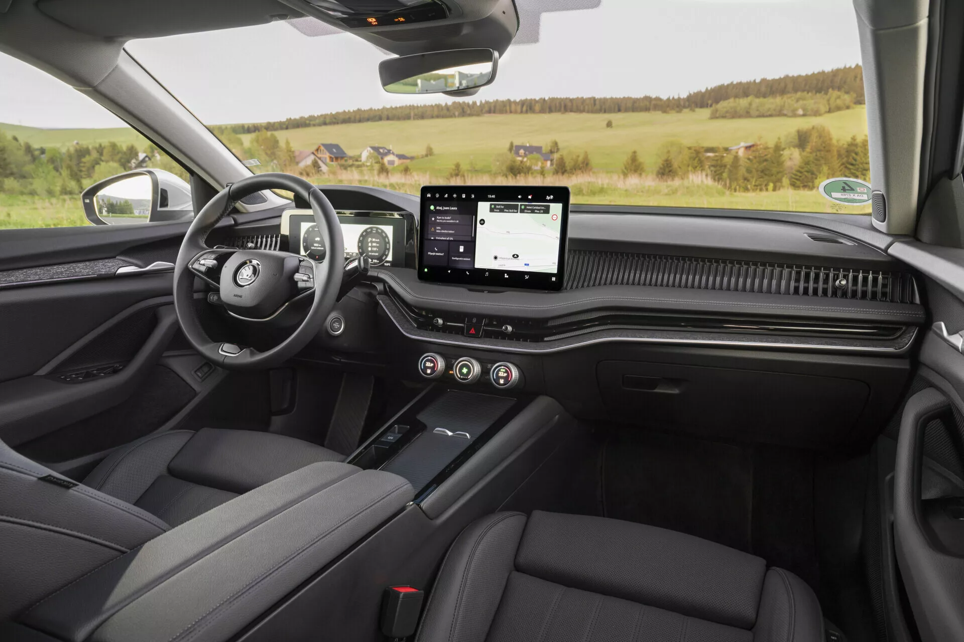 Interiörvy av Skoda Superb 2024 limousine från baksätet, som visar den främre instrumentpanelen, förar- och passagerarsäten i svart läder, central konsol med växelspak, pekskärmsinfotainmentsystem, fullständigt digital instrumentpanel, kolfiberaccenter och en lugn semilandsbygdsmiljö utanför.