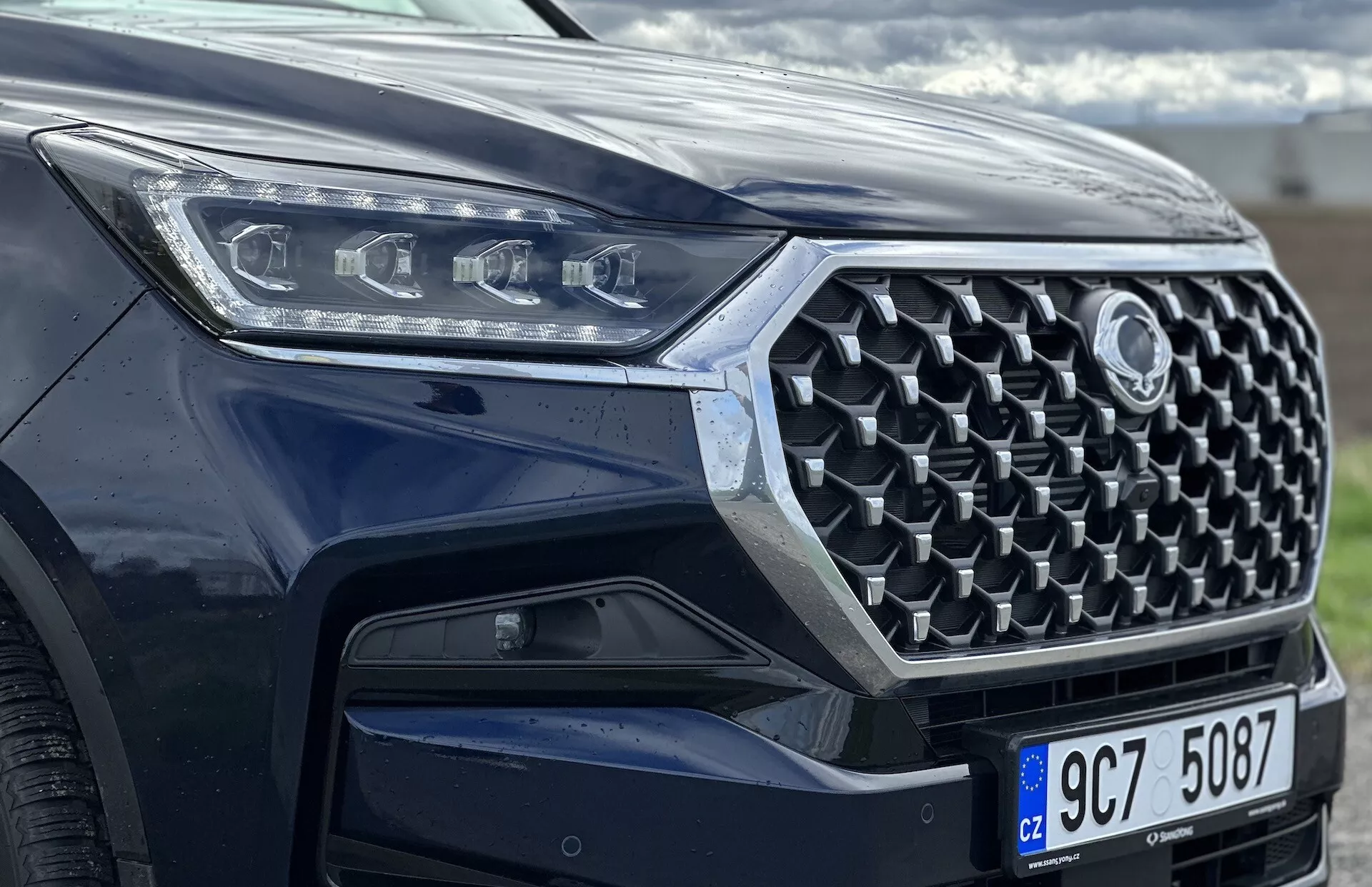 Framifrån vinklad vy av en SsangYong Rexton 2021 med fokus på grill, frontstötfångare och LED-strålkastardesign, som visar avancerade säkerhetsfunktioner och modern teknik med metallisk kroppsfärg.