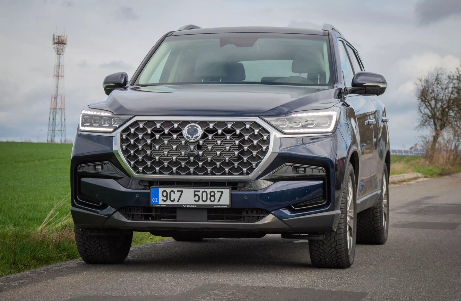 SUV SsangYong Rexton 2021 på landsväg, som visar en detaljerad vy av dess frontdesign med ett geometriskt grill och LED-strålkastare, som återspeglar avancerad teknik och terrängförmåga