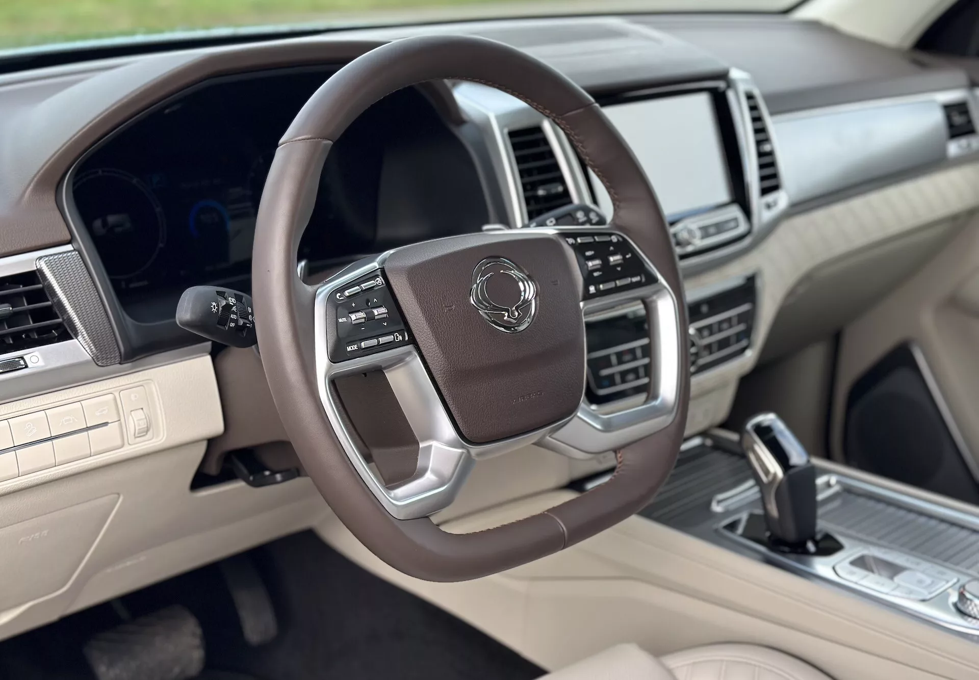 2021 SsangYong Rextons lyxiga interiörvy från främre passagerarsidan, med en multifunktionell läderklädd ratt med metalliska accenter, digital instrumentpanel, avancerat infotainmentsystem och ett tvåtonat beige och mörkt färgschema.