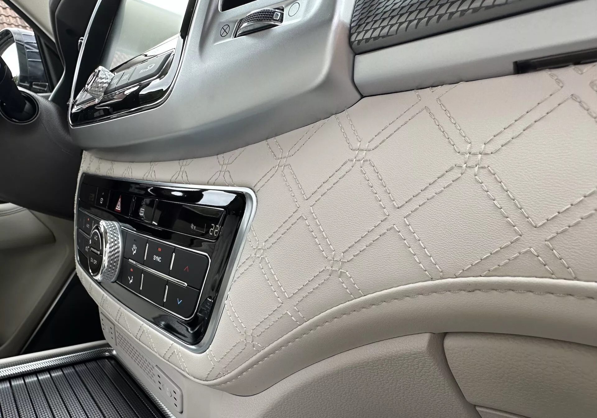 2021 SsangYong Rexton interiör som fokuserar på passagerarsidans instrumentbräda och en del av främre dörrpanelen med diamantstickat läder, infotainment-kontroller och lyxiga trädetaljer