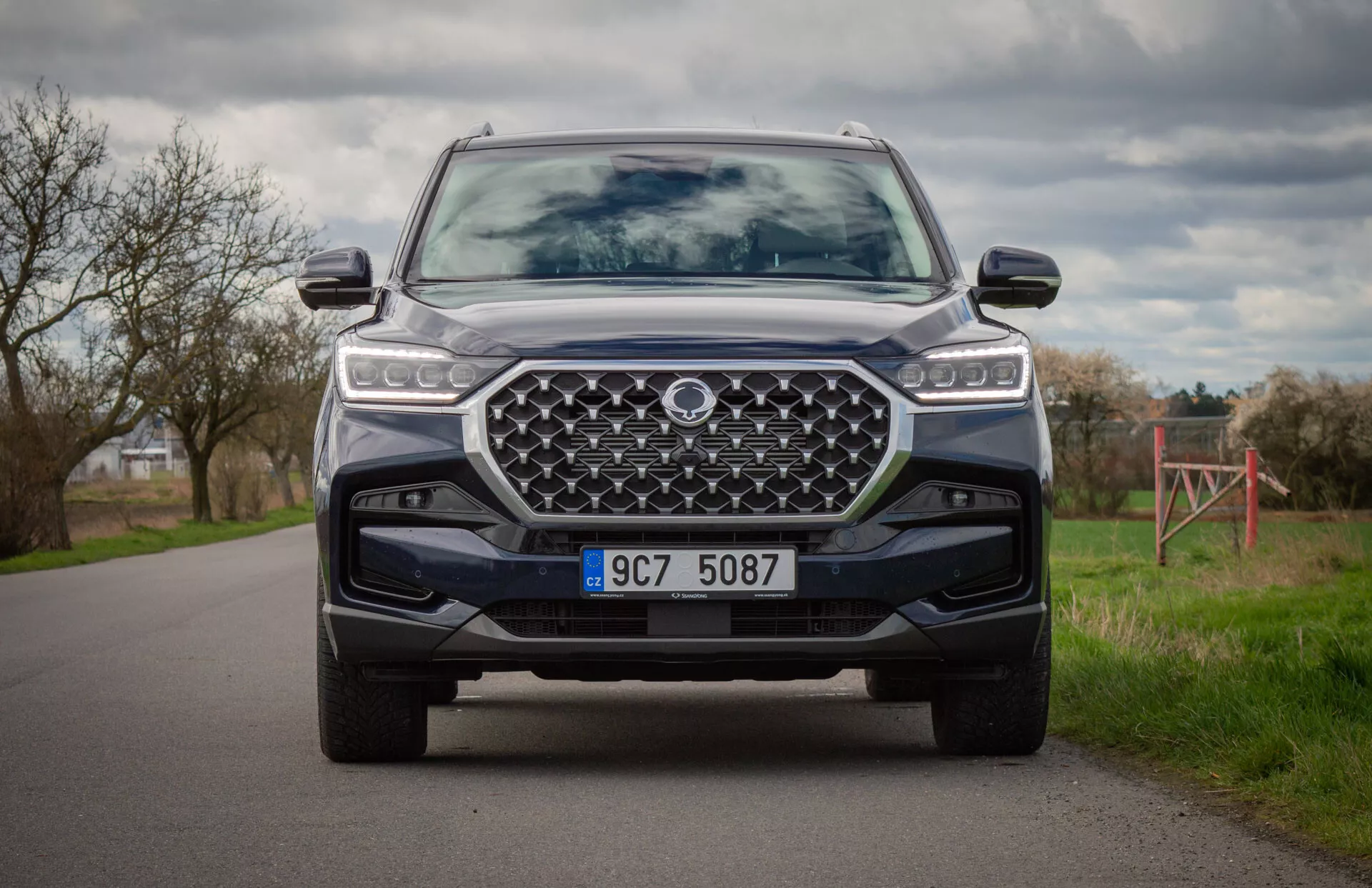 Modern SUV SsangYong Rexton 2021 i färg, fångad från knästående position som visar fordonets front, LED-strålkastare, stor designad grill, frontstötfångare med skidplåt och avancerade förarassistanssystem