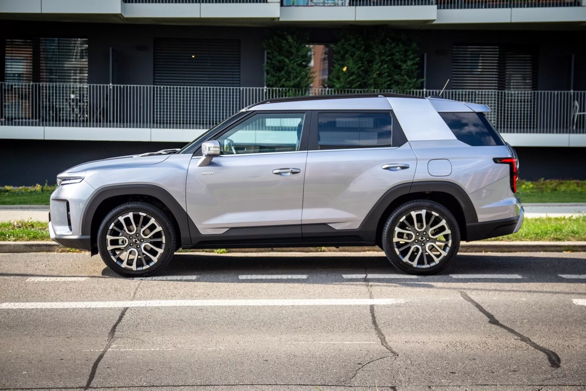 Sidoprofil av SsangYong Torres 2023 som visar dess kantiga men ändå aerodynamiska design, högt midjeband, platt tak och ljusmetallisk färg med fälgar i femekert legering, karossfärgade sidospeglar med integrerade blinkers, lätt tonade rutor, dörrhandtag i linje med karossen och svart skyddslist på en solig gata