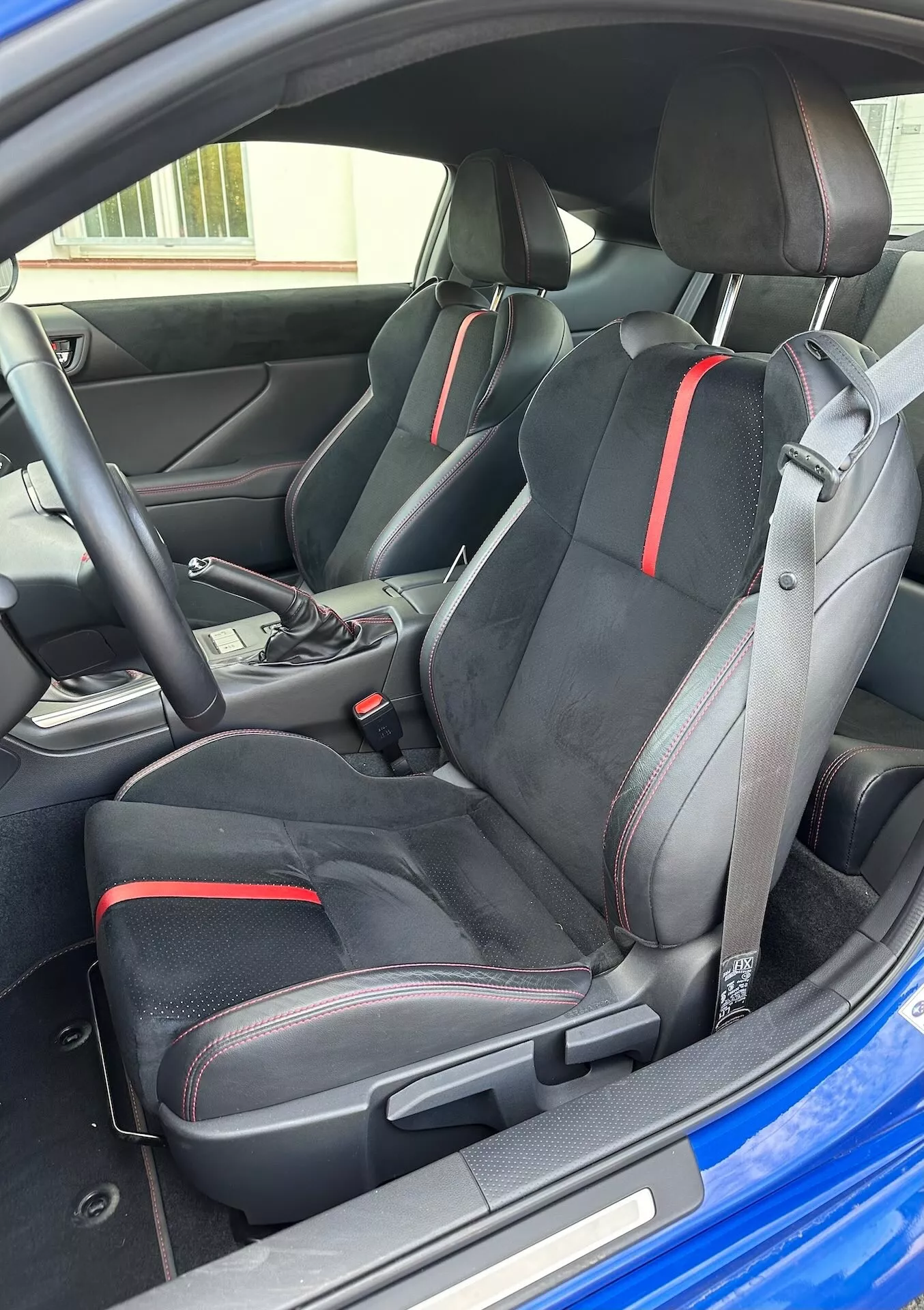 Interiörvy av Subaru BRZ 2023 som framhäver de sportiga framsätena med ergonomisk design och röda detaljer, väljare för automatväxellåda och modern cockpitestetik från ett snett yttre perspektiv
