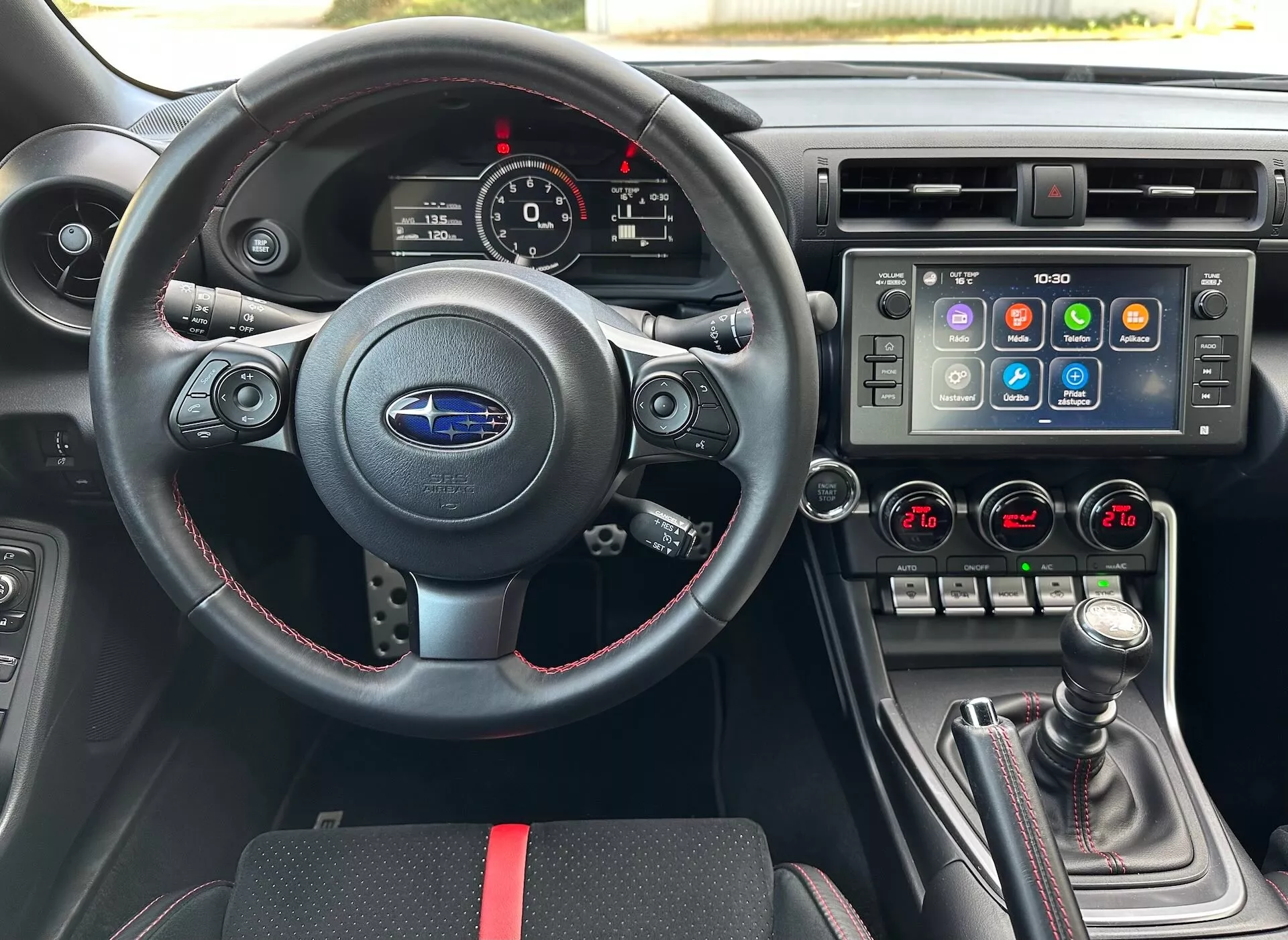 Interiör av Subaru BRZ 2023 från förarens perspektiv inklusive en sportig läderratt med multifunktionskontroller och röda sömmar, en instrumentkluster med analoga urtavlor och en digital display, en mittkonsol med en stor pekskärms infotainmentsystem och dubbelzons klimatkontroll, samt en manuell växelspak med läderöverdrag och röda accenter, mot en svart interiör med sportiga röda accenter, som framhäver avancerade fordonsegenskaper och teknologi.