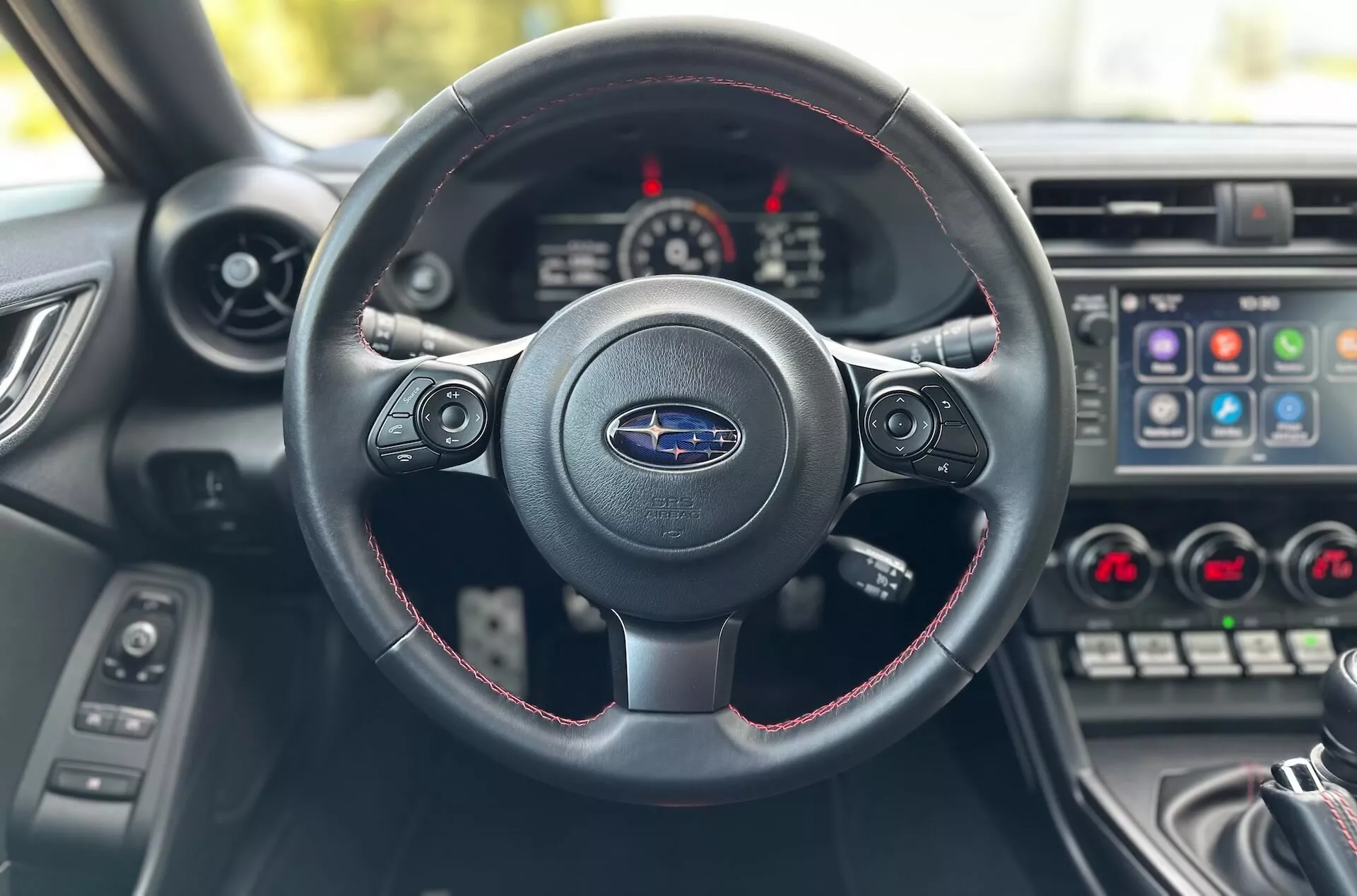 Interiörvy av Subaru BRZ 2023 från förarsätet med fokus på tre-ekrad ratt med röda sömmar, Subaru-logotyp, och instrumentbräda med instrumentkluster och mittkonsol
