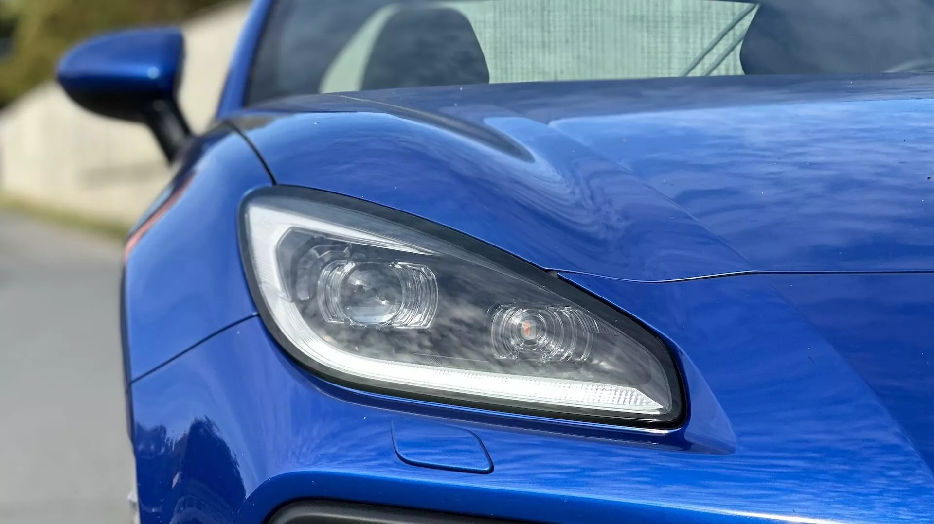 Närbild av förarsidans strålkastare på Subaru BRZ 2023, med LED- eller HID-belysning, projektorlinser, och en sportig luftintag mot en metallisk blå kaross