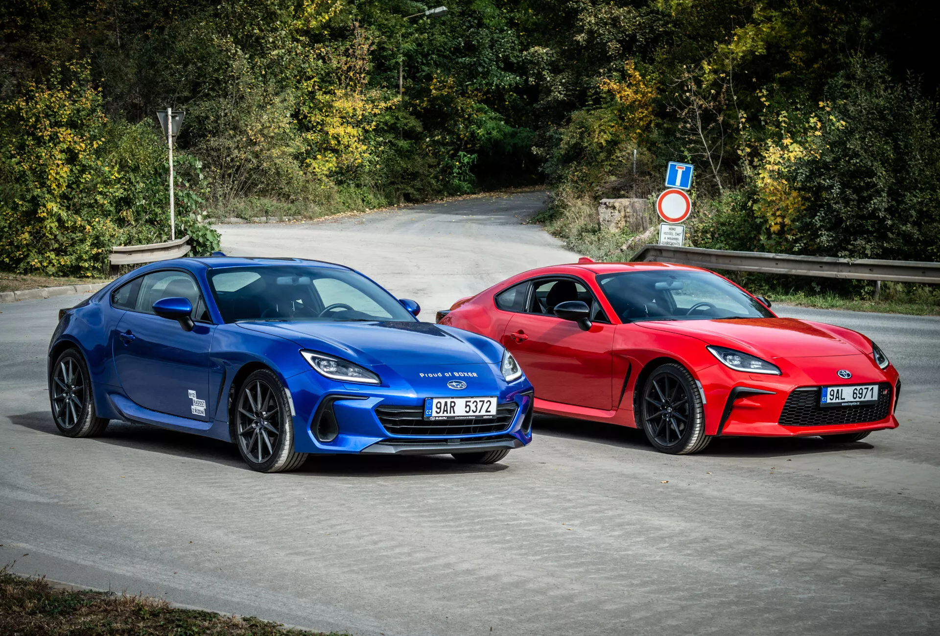 Sportiga coupéer Subaru BRZ 2023 i blått och rött med aerodynamisk design och prestandaegenskaper, parkerade utomhus omgivna av naturlig lövverk