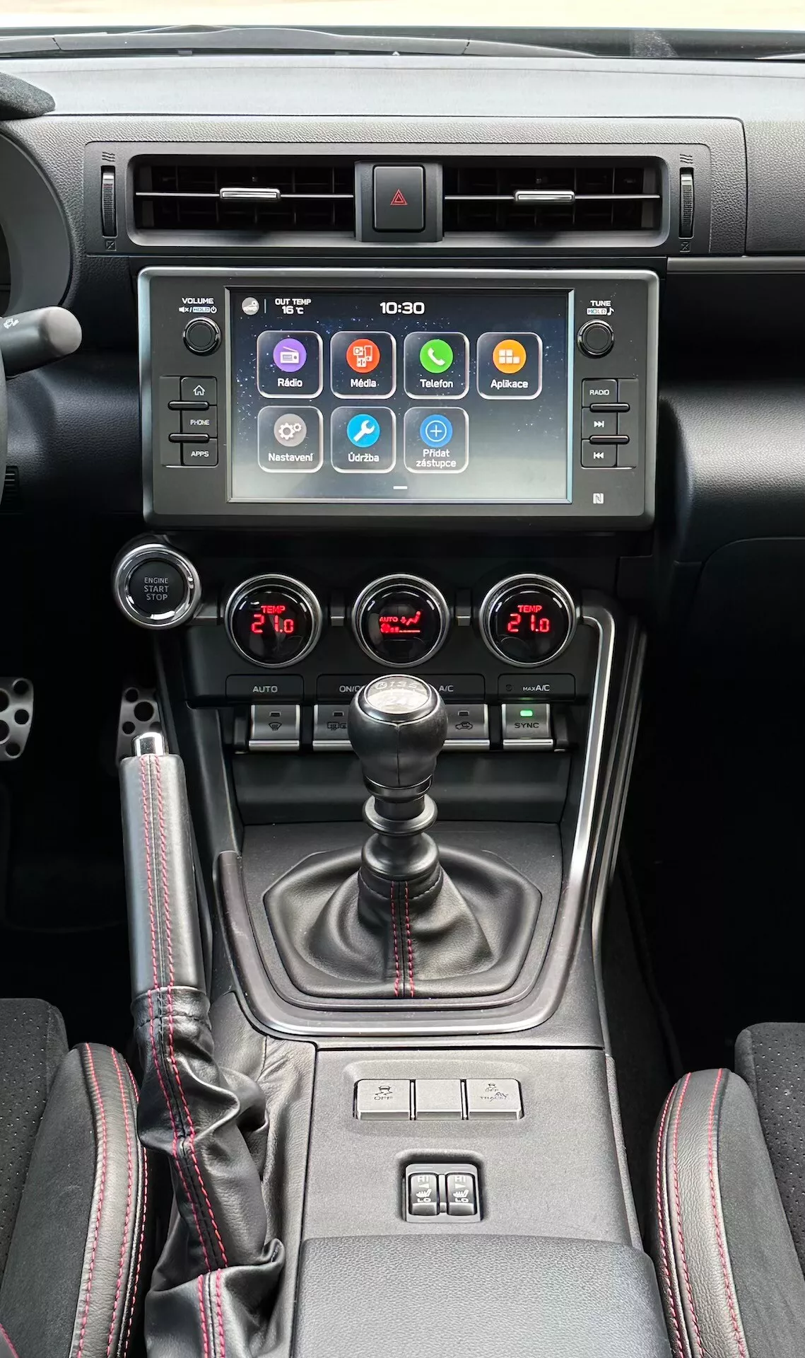 2023 Subaru BRZ interiör som visar den centrala konsolen, med en pekskärmsdisplay för underhållningssystemet, varningsljusindikator, metalliska luftventiler, dubbelzons klimatkontroll, manuell växelspak med läderkåpa, stolsvärmningskontroller och en flerlägeskörningsväljare i en modern svart och metallisk design.