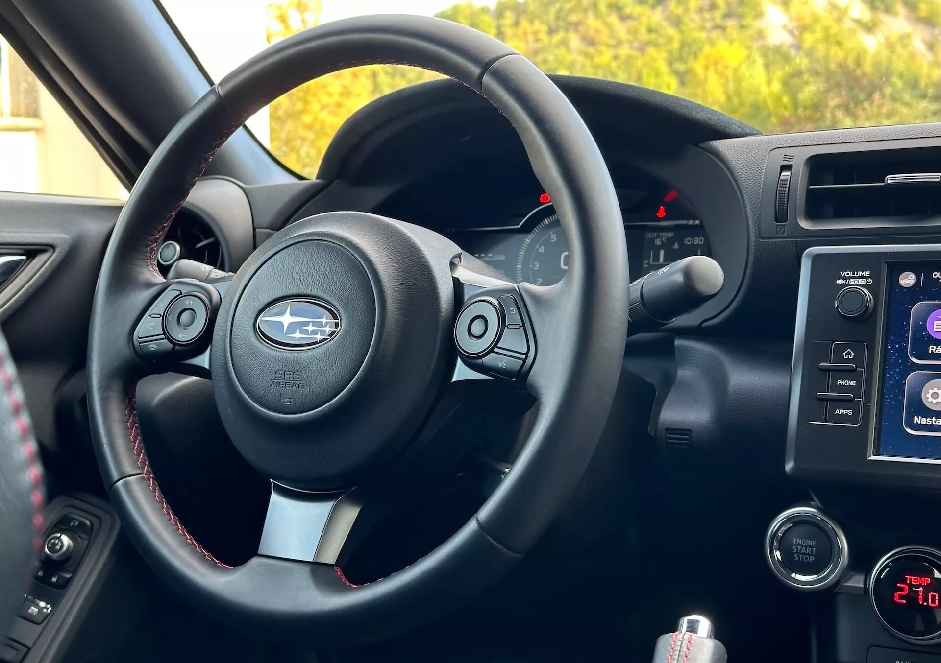Interiörvy av Subaru BRZ 2023 från passagerarperspektiv som visar ratten med metalliska accenter och Subaru-logotyp, kontrollknappar, kontrastsömmar, instrumentkluster med belysta indikatorer, mittkonsolens infotainmentsystem, ljud- och klimatkontroller och förvaringsfack.