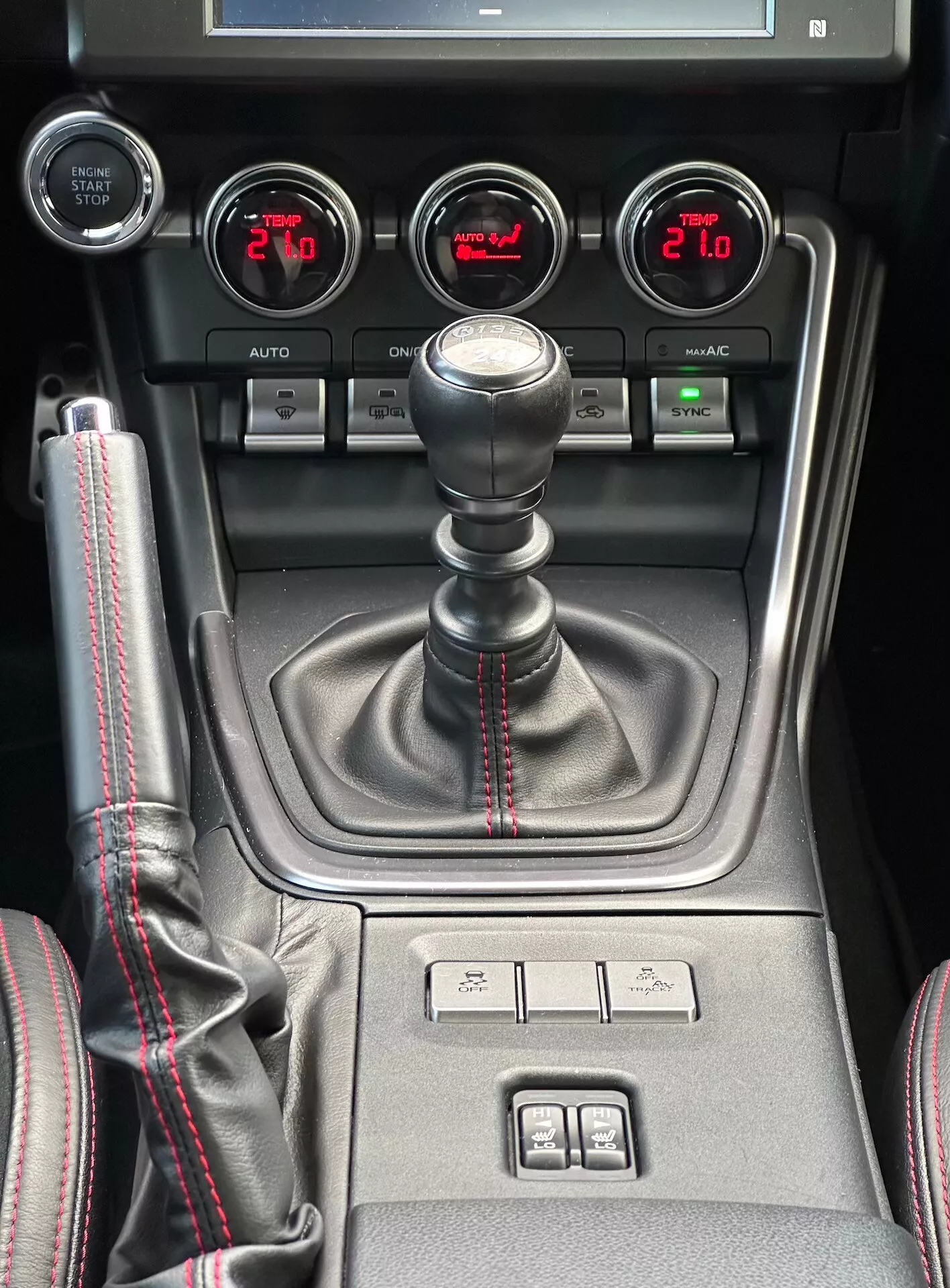 Central konsol i Subaru BRZ 2023 med manuell växelspak med sportig röd söm, hjälpinstrument för turbo tryck, batterispänning, oljetemperatur och dubbelzons klimatkontroll i detaljerad interiörvy