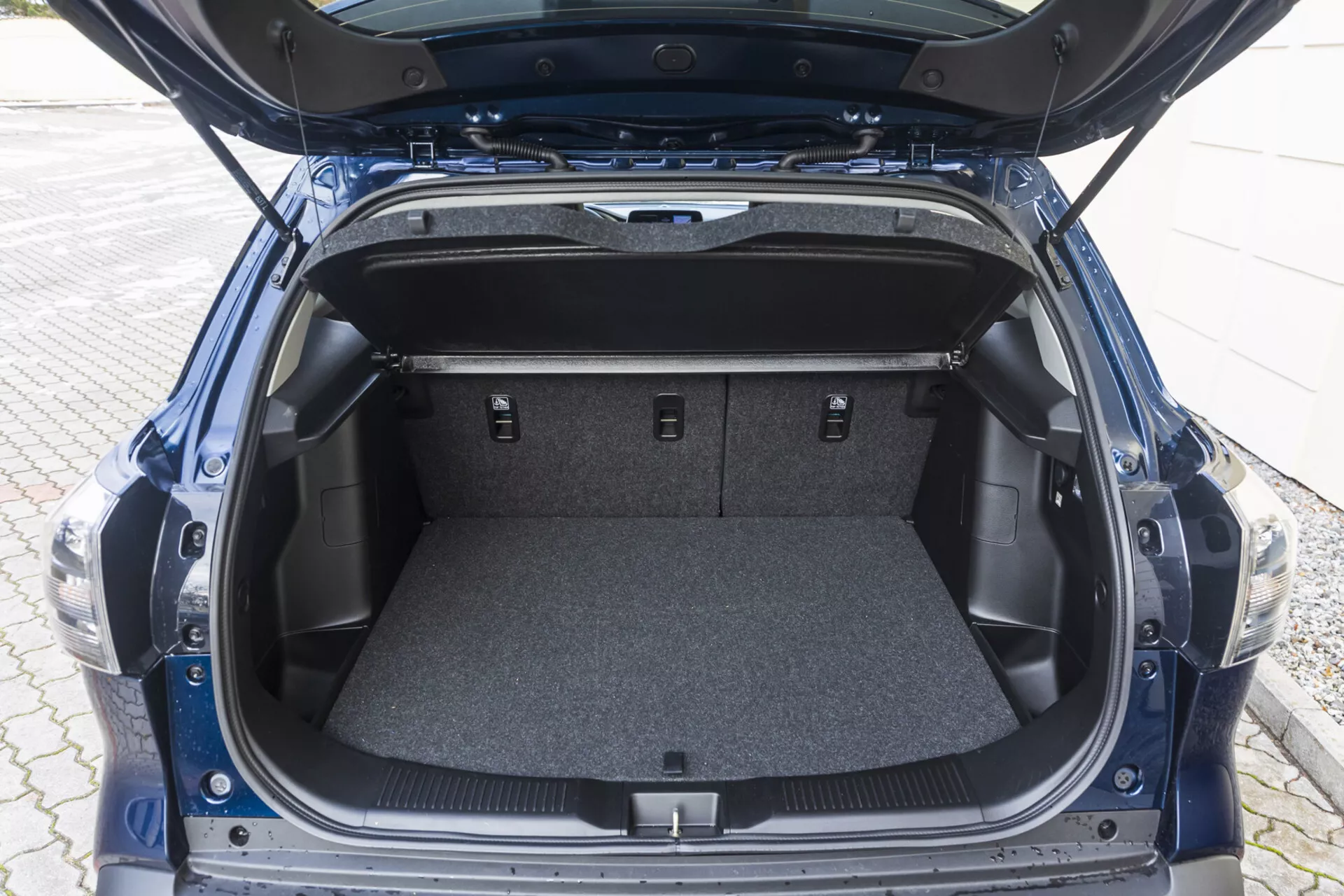 Vy över 2022 Suzuki S-Cross bakre bagageutrymme med öppet lock som visar tomt mattat område, sidofack och nedfällda baksäten