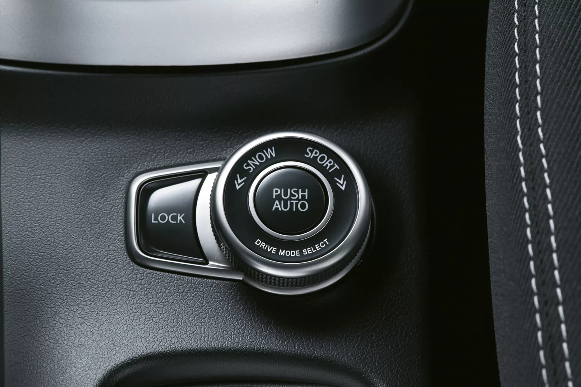 Närbild på interiören i Suzuki S-Cross 2022 som visar växellägesväljaren märkt 'PUSH AUTO' med alternativen 'SNOW' och 'SPORT', bredvid en 'LOCK'-knapp, på en högkvalitativ mörkt tonad panel, möjligen med läderliknande textur och synliga sömmar.
