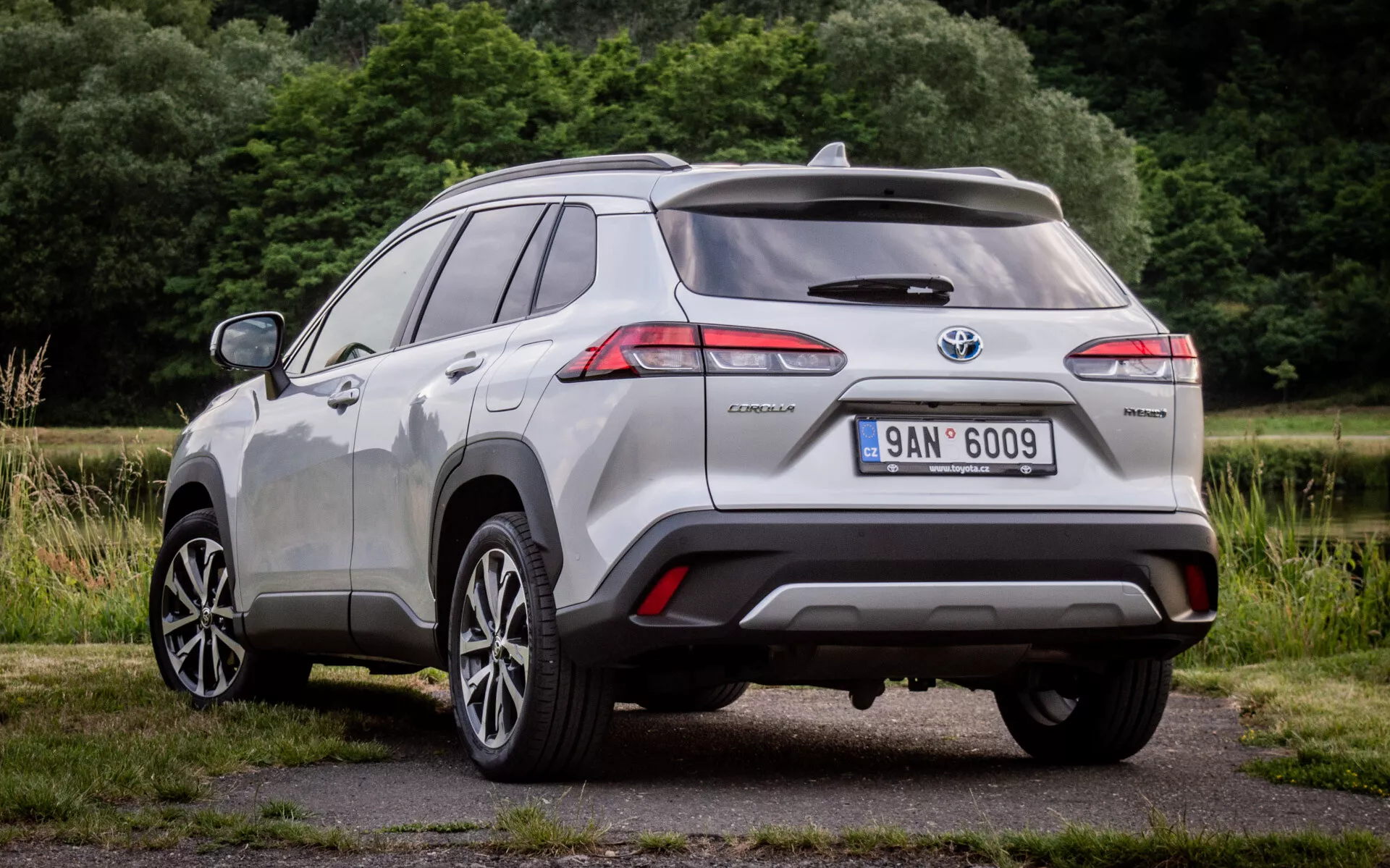 Bakre tre fjärdedels vyn av Toyota Corolla Cross 2022 som visar LED-bakljus, hybridmärke och parkeringshjälpssensorer