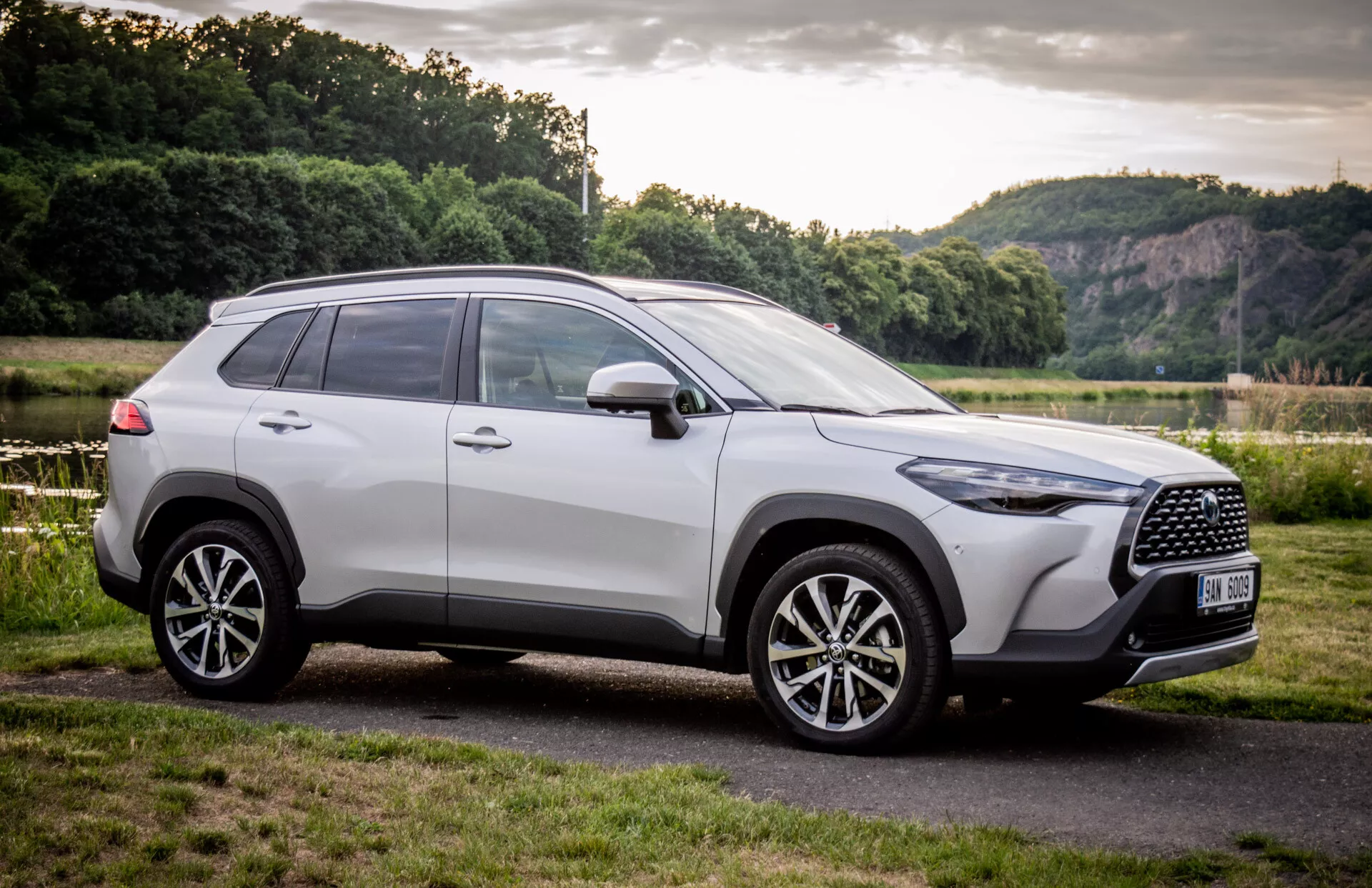 SUV Toyota Corolla Cross 2022 parkerad utomhus, visar upp sin moderna design från en tredjedels frontalvinkel med fokus på grillen, legeringshjulen och sidprofilen mot en naturbakgrund