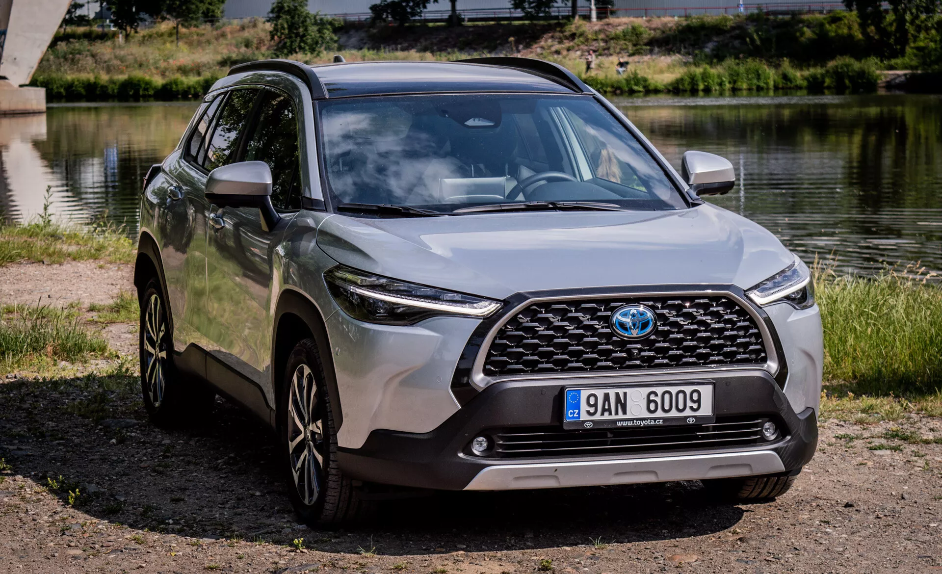 2022 Toyota Corolla Cross modern crossover SUV parkerad utomhus nära en vattenkropp med tydlig vy över dess frontgrill, huven, LED-strålkastare, frontkofångare och sidoprofil inklusive legeringshjul och karossfärgade sid-spegel