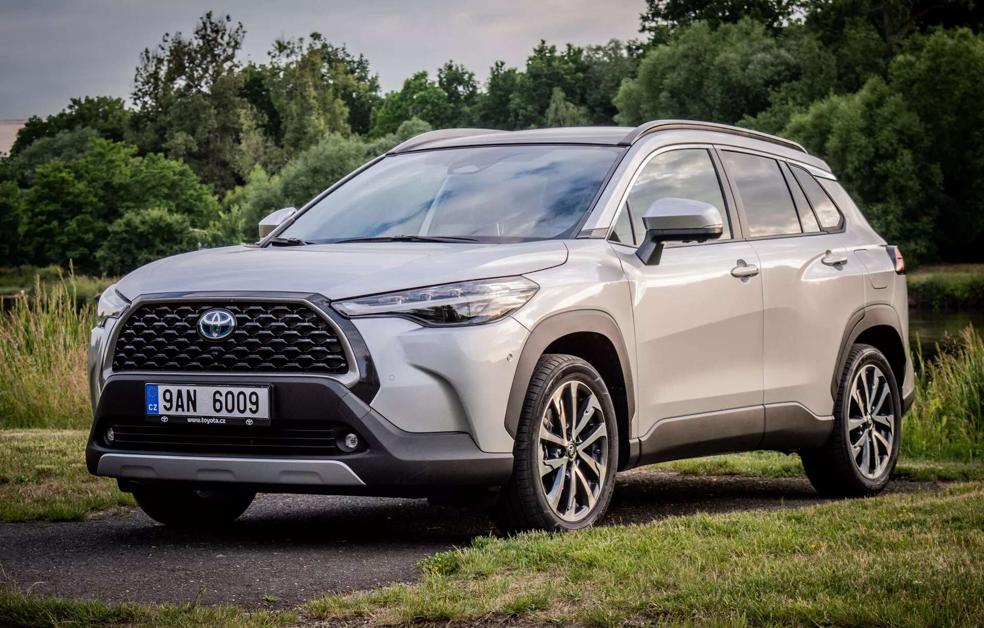 Toyota Corolla Cross 2022 som visar upp sin dynamiska design med ett tre kvarts främre perspektiv, framhäver den stora mönstrade frontgrillen, smidiga LED-strålkastarenheter och flerspakiga legeringshjul, parkerad i en naturlig parkmiljö