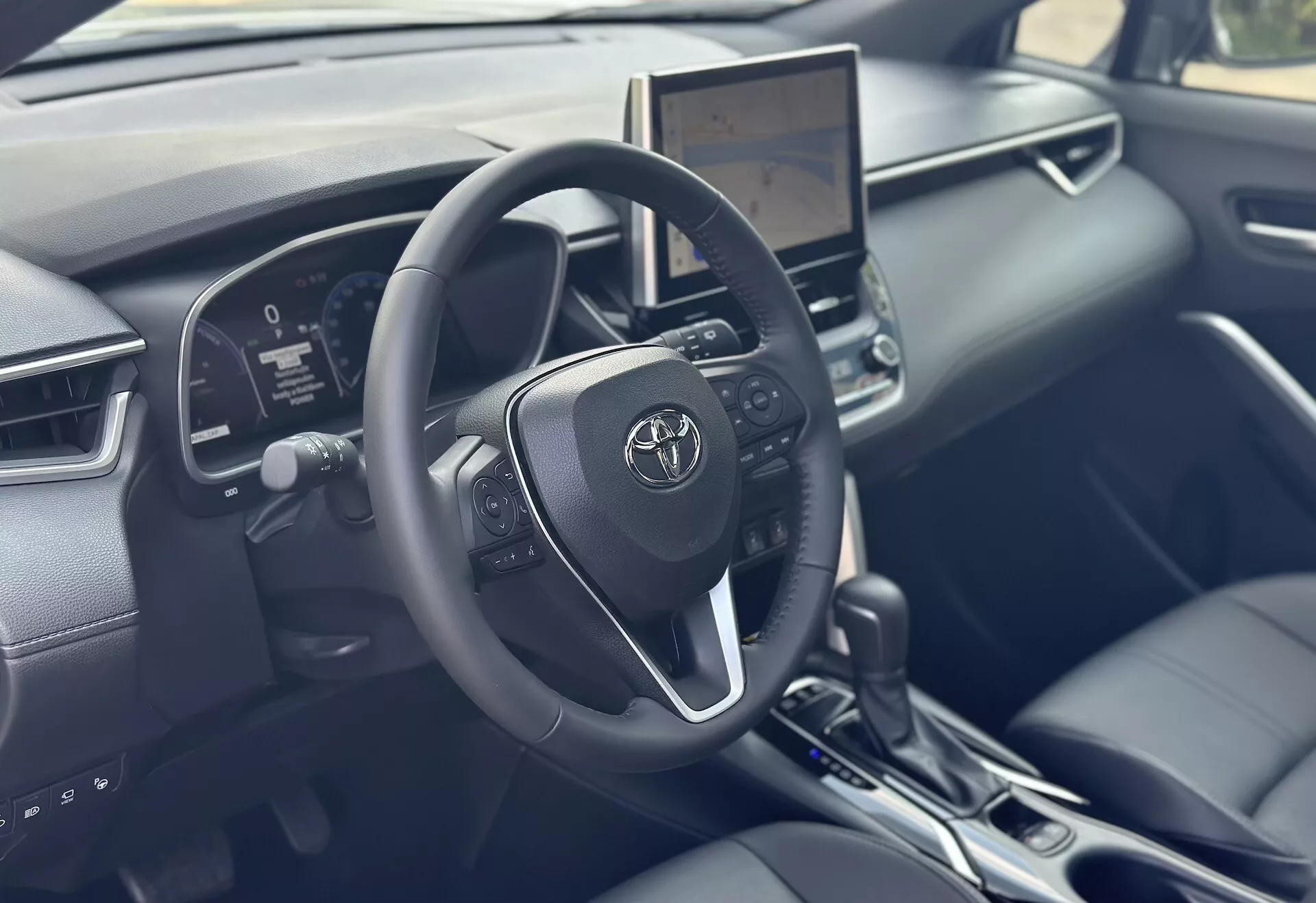 Interiör av Toyota Corolla Cross 2022 med fokus på förarsidan med detaljerat ratt, digital instrumentkluster och central infotainment pekskärm med modern teknik och svarta läderdetaljer