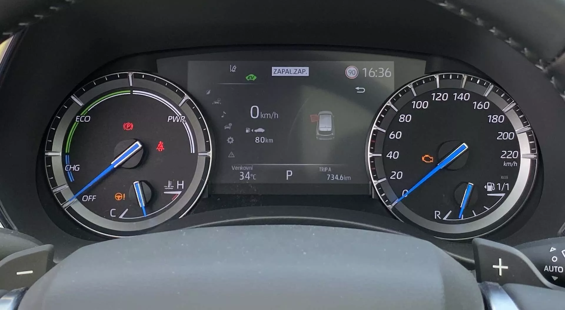 Digital-analog hybrid instrumentbräda i en Toyota Highlander 2021, sedd från förarsätet, med en varvräknare med ECO-lägesindikator till vänster, en hastighetsmätare med bränslenivåindikator till höger och en central digital display som visar hastighet (0 km/h), utomhustemperatur (34°C), klocka (16:36) och en ikon för förarassistanssystemet.