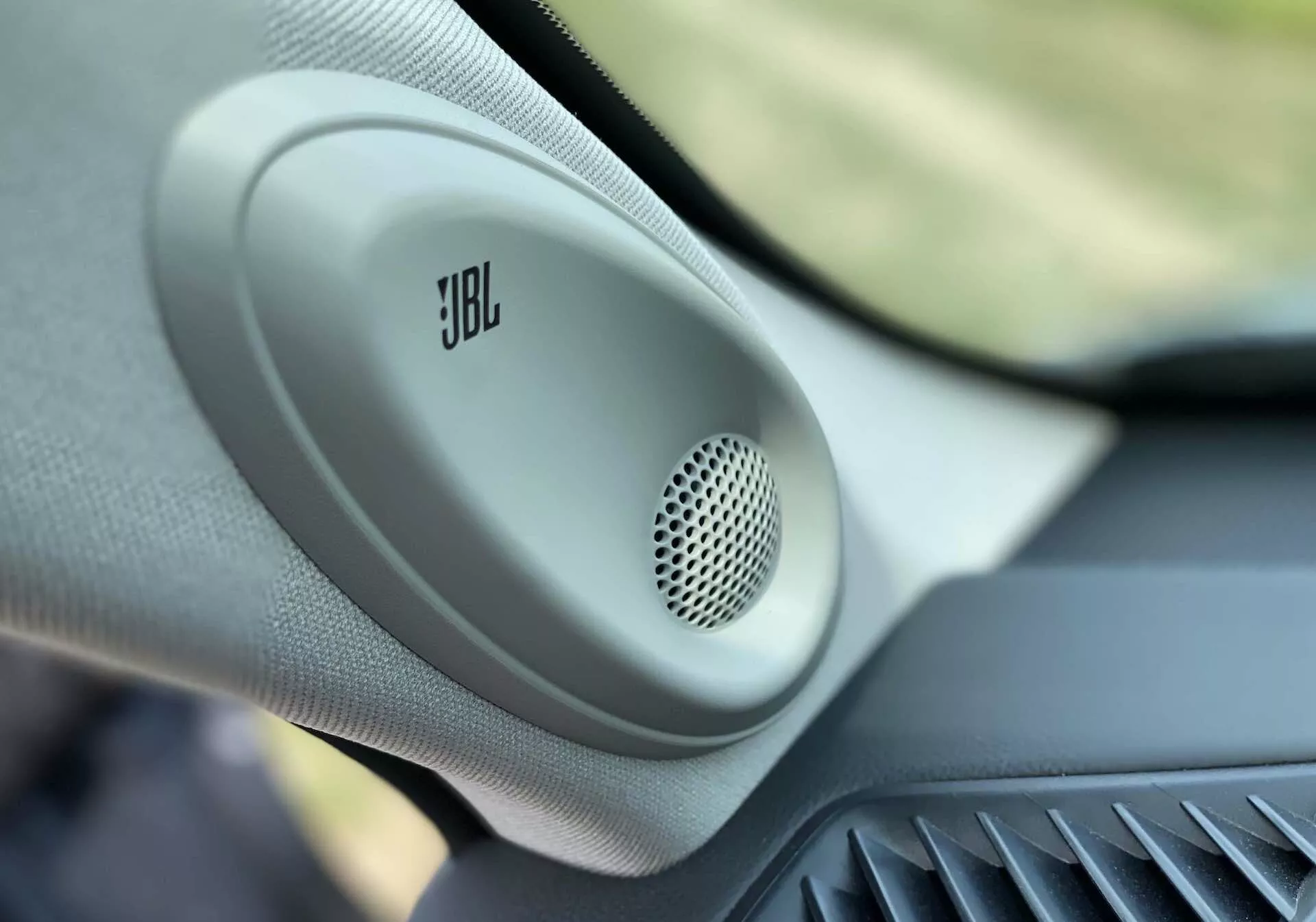 Närbild av interiören i 2021 Toyota Highlander 2.5 Hybrid Business Edition, som framhäver en dörrmonterad JBL-högtalare med ett cirkulärt nätgaller och texturerat hölje och betonar premiumbilens ljudsystem och lyxbilens funktioner.