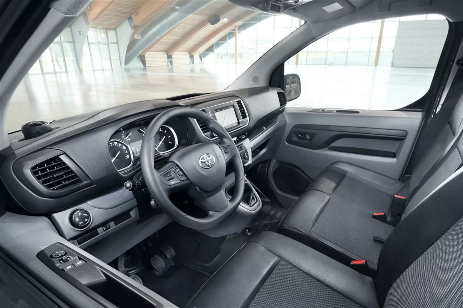Närbild på interiören i en Toyota Proace Verso från 2016 från förarsidan, med detaljvy av instrumentbrädan, ratten med Toyota-logotypen och monterade kontroller, instrumentklustret och underhållningssystemet